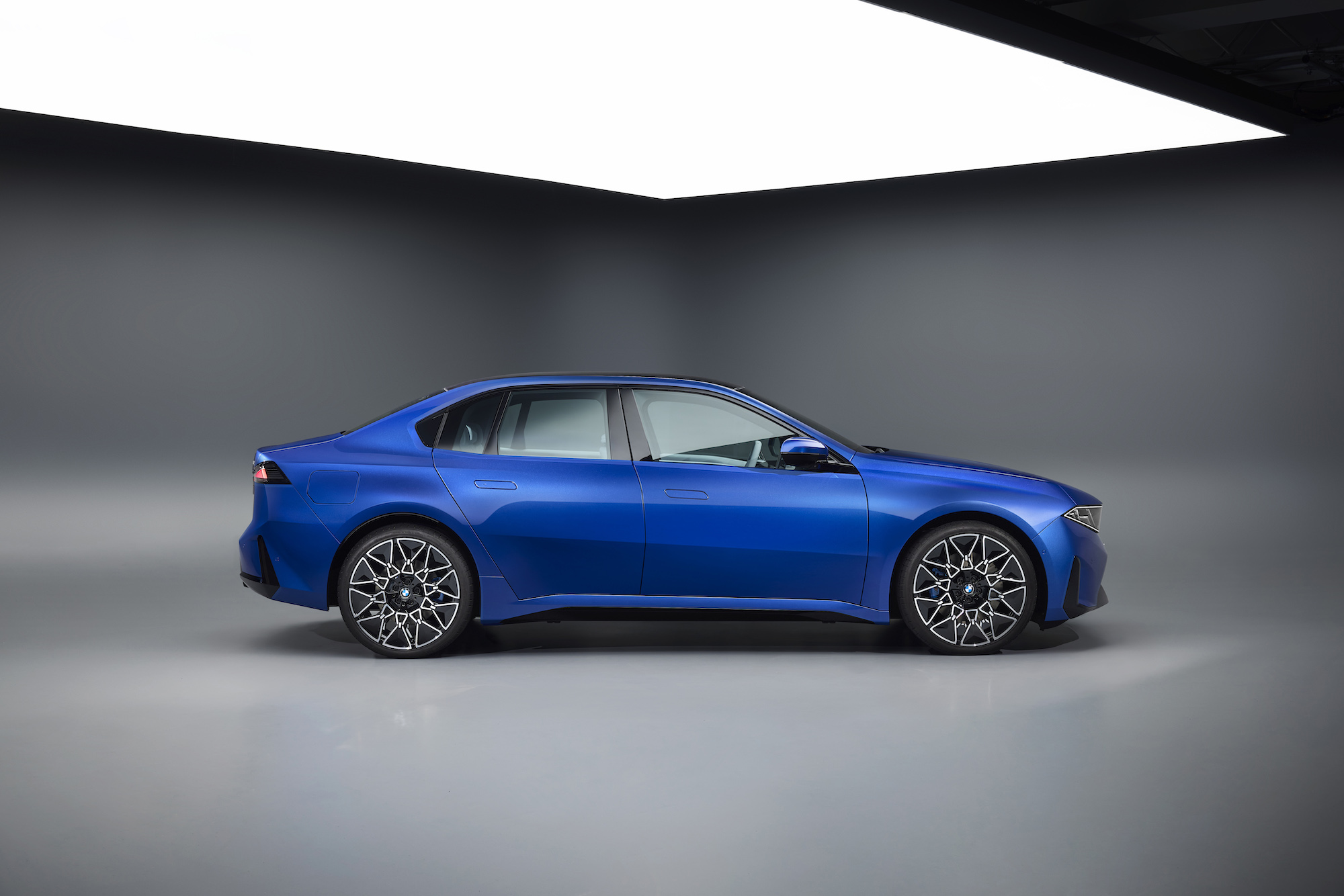 Side view of a blue modern car with sleek design, featuring sporty wheels, set against a minimalist backdrop.