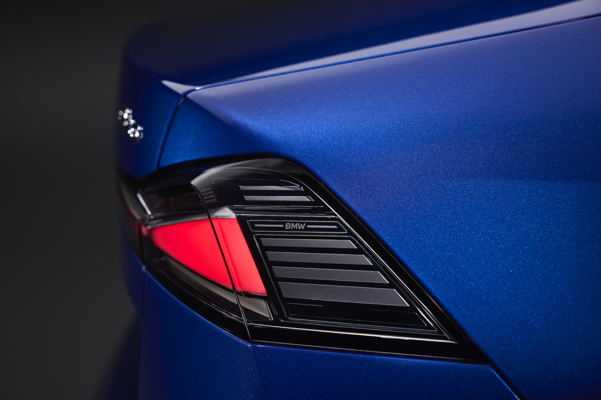 Close-up of a BMW car's rear light on a vibrant blue surface.