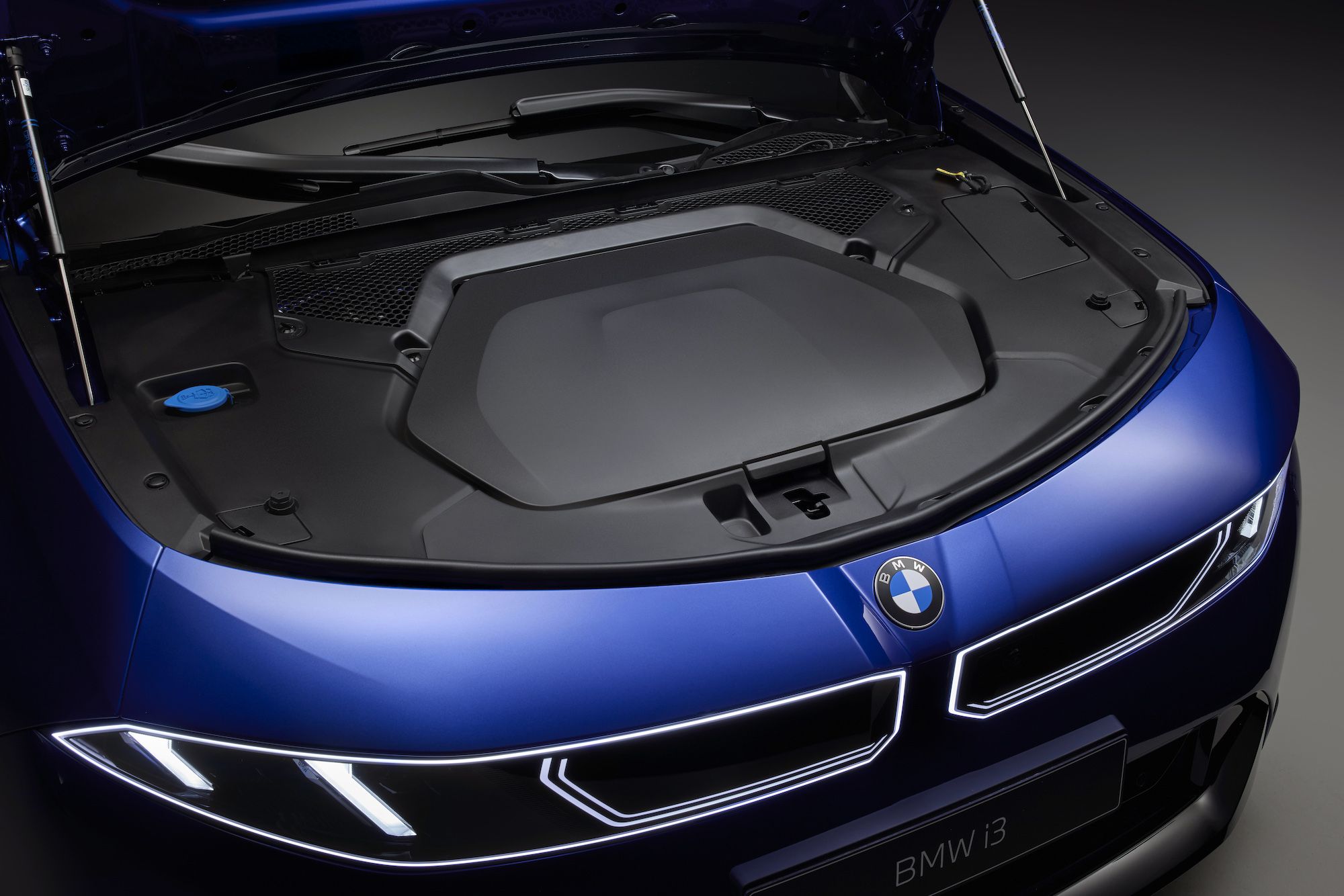 Close-up view of the engine compartment of a BMW i3, showcasing the blue engine cover and components under the hood.