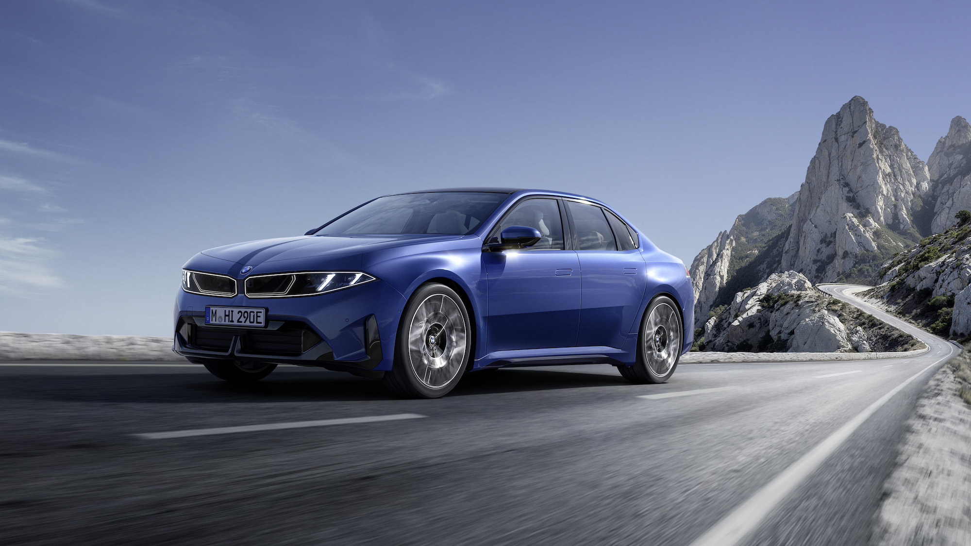 A blue BMW sedan driving on a winding road with mountainous scenery in the background.