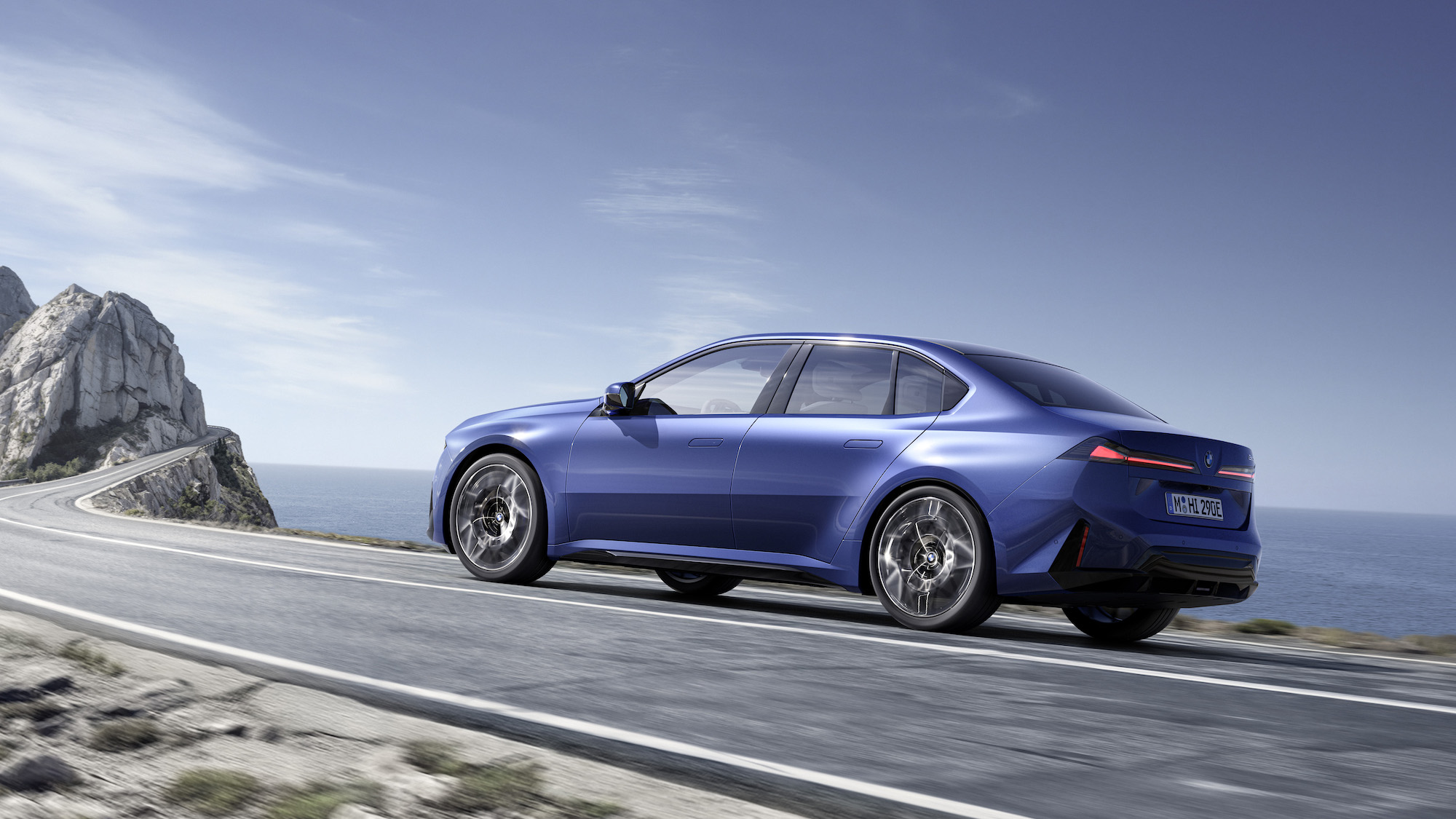 A sleek blue car driving along a winding coastal road with cliffs and ocean views.