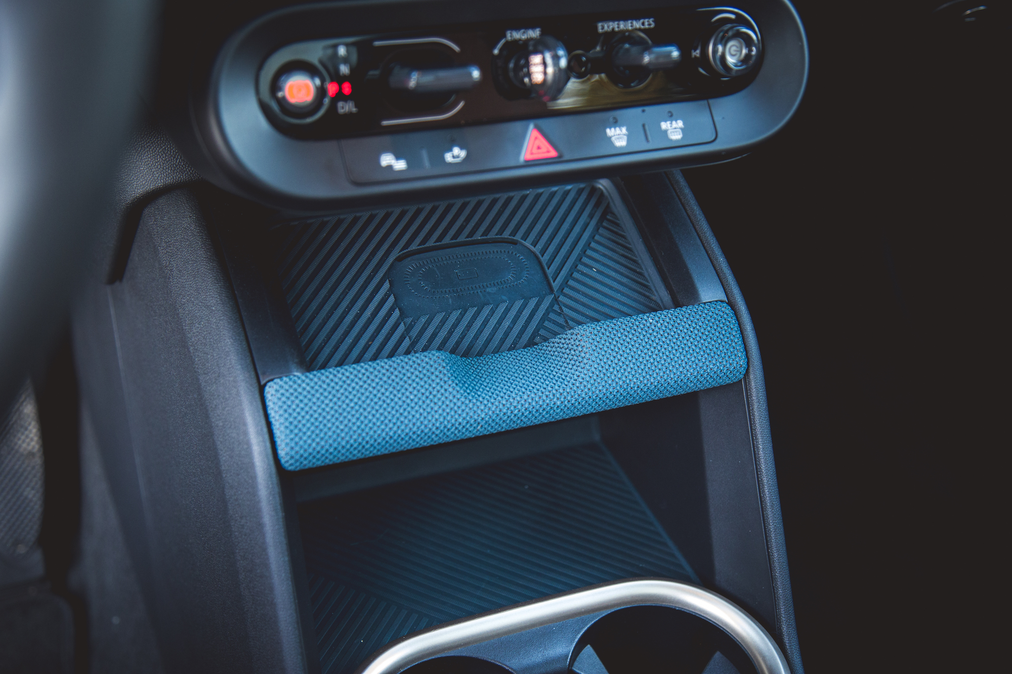 Close-up of a car's center console featuring a textured black surface with a blue padded grip and control buttons above.