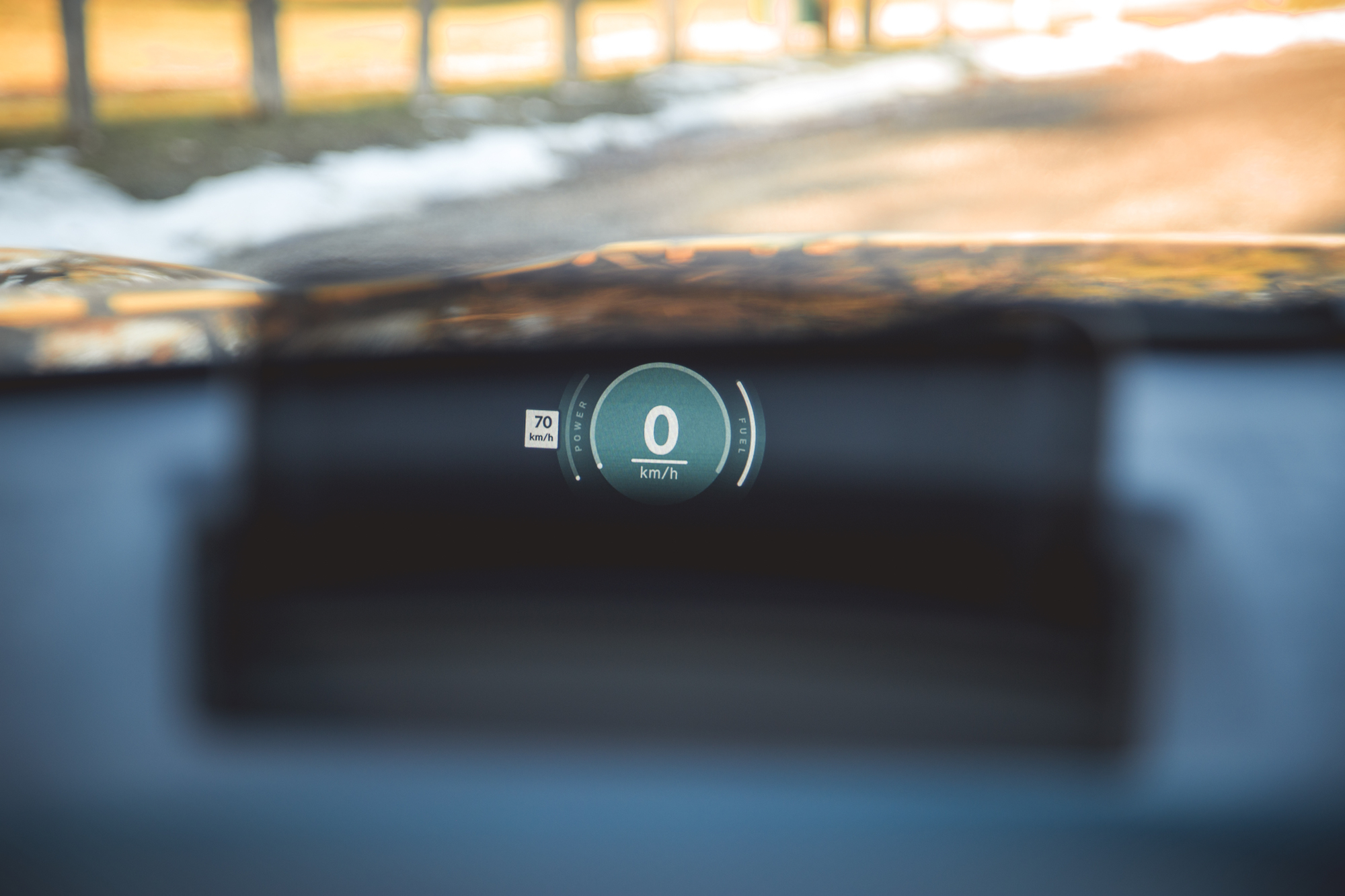 Close-up of a car's digital speedometer showing 0 km/h with a speed limit sign of 70 km/h in the background.