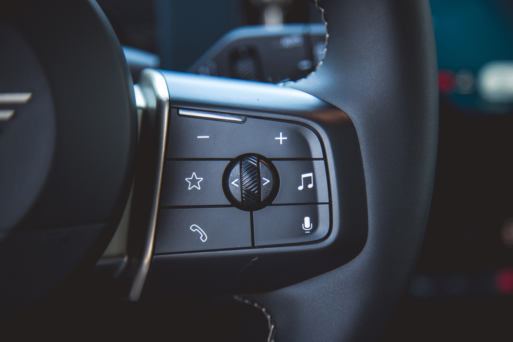 Close-up of a car steering wheel control panel featuring buttons for phone, music, favorites, and voice commands.