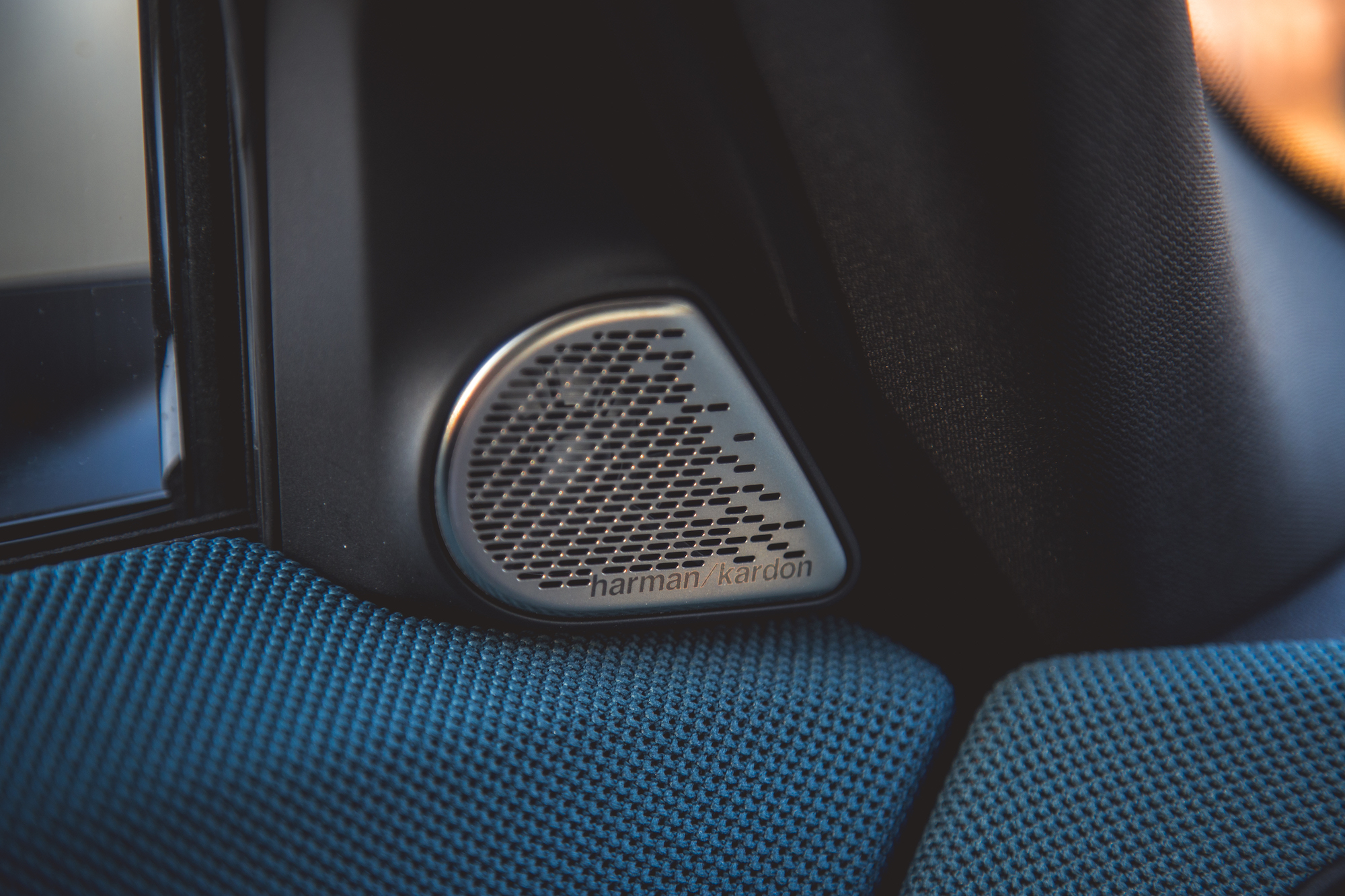 Close-up of a Harman Kardon speaker embedded in a car's interior featuring blue fabric upholstery.