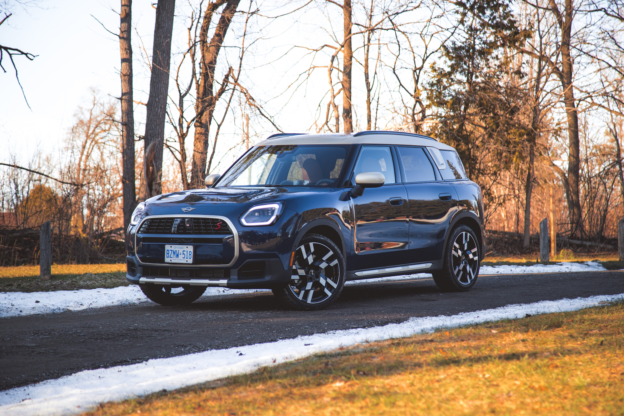 A sleek blue SUV parked on a gravel path surrounded by trees and a hint of snow on the ground.