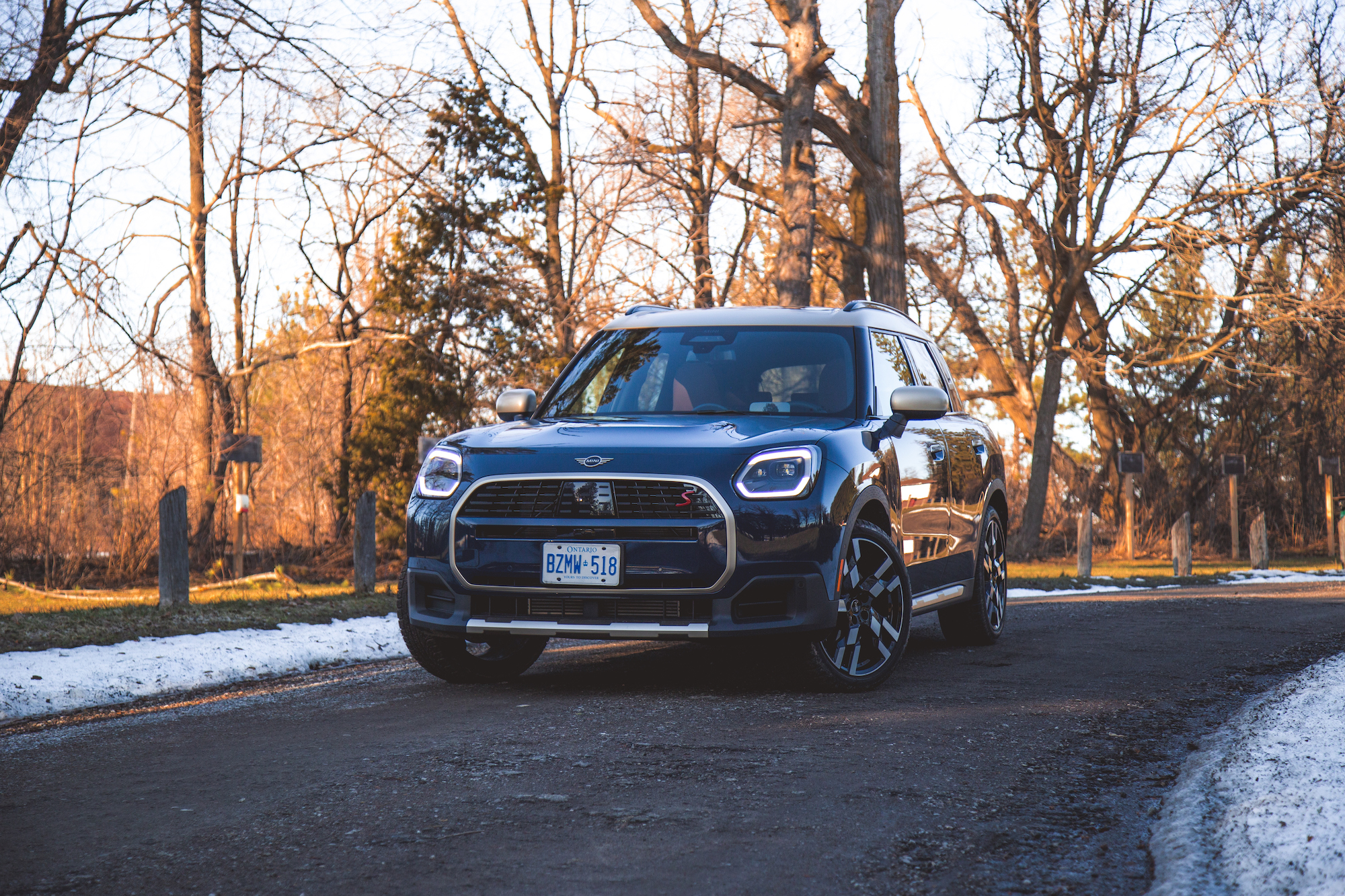 A blue SUV parked on a gravel road surrounded by trees, with snow visible in some areas.