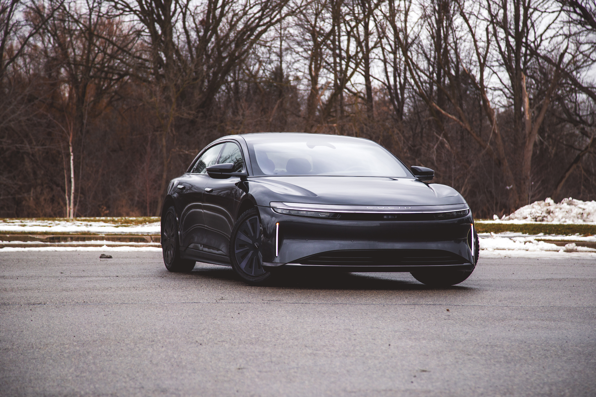 Un elegante coche eléctrico negro estacionado sobre una superficie pavimentada con árboles al fondo.
