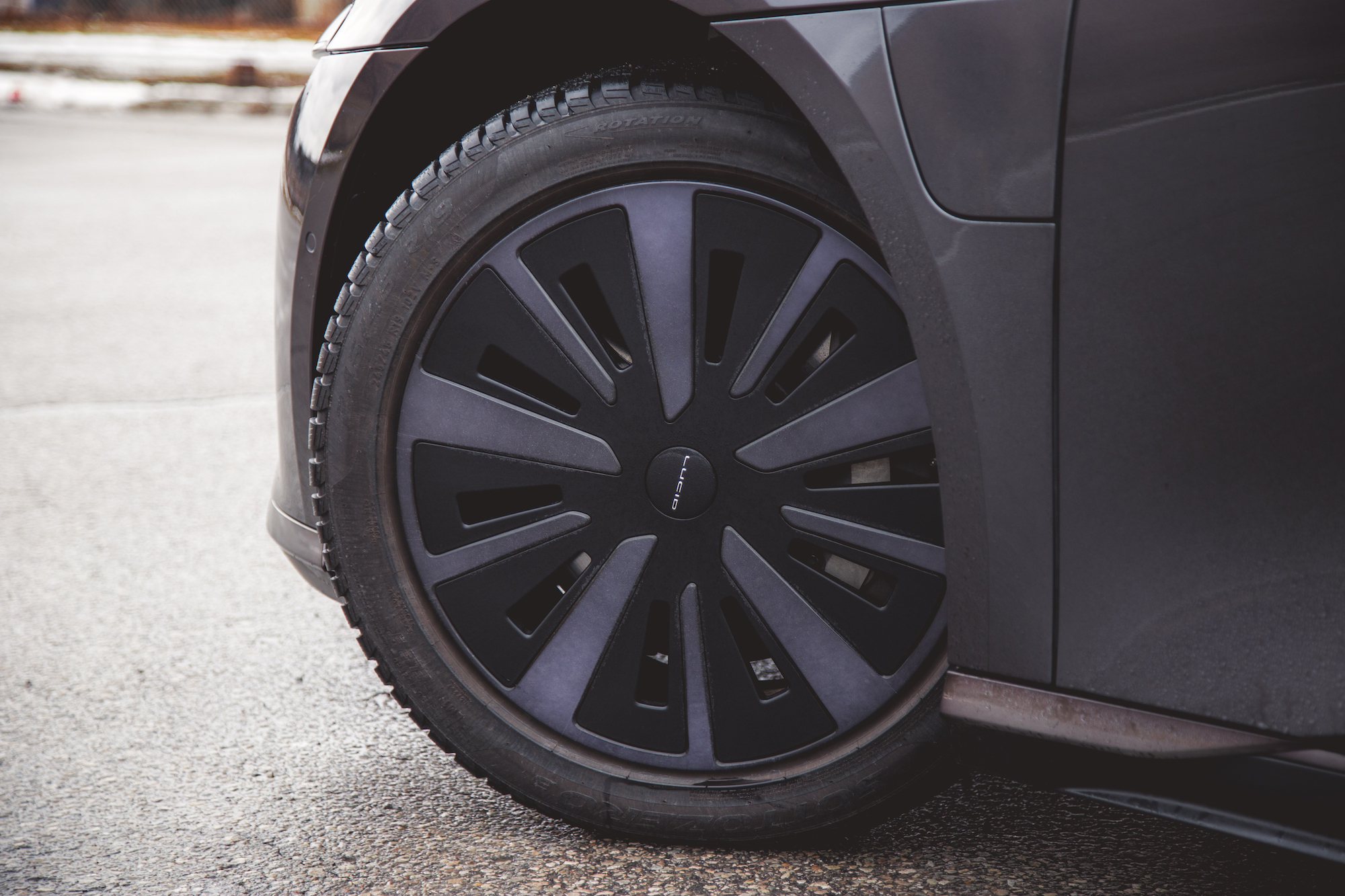 Primer plano de la rueda negra de un automóvil con un diseño único, parcialmente visible sobre una superficie texturizada.