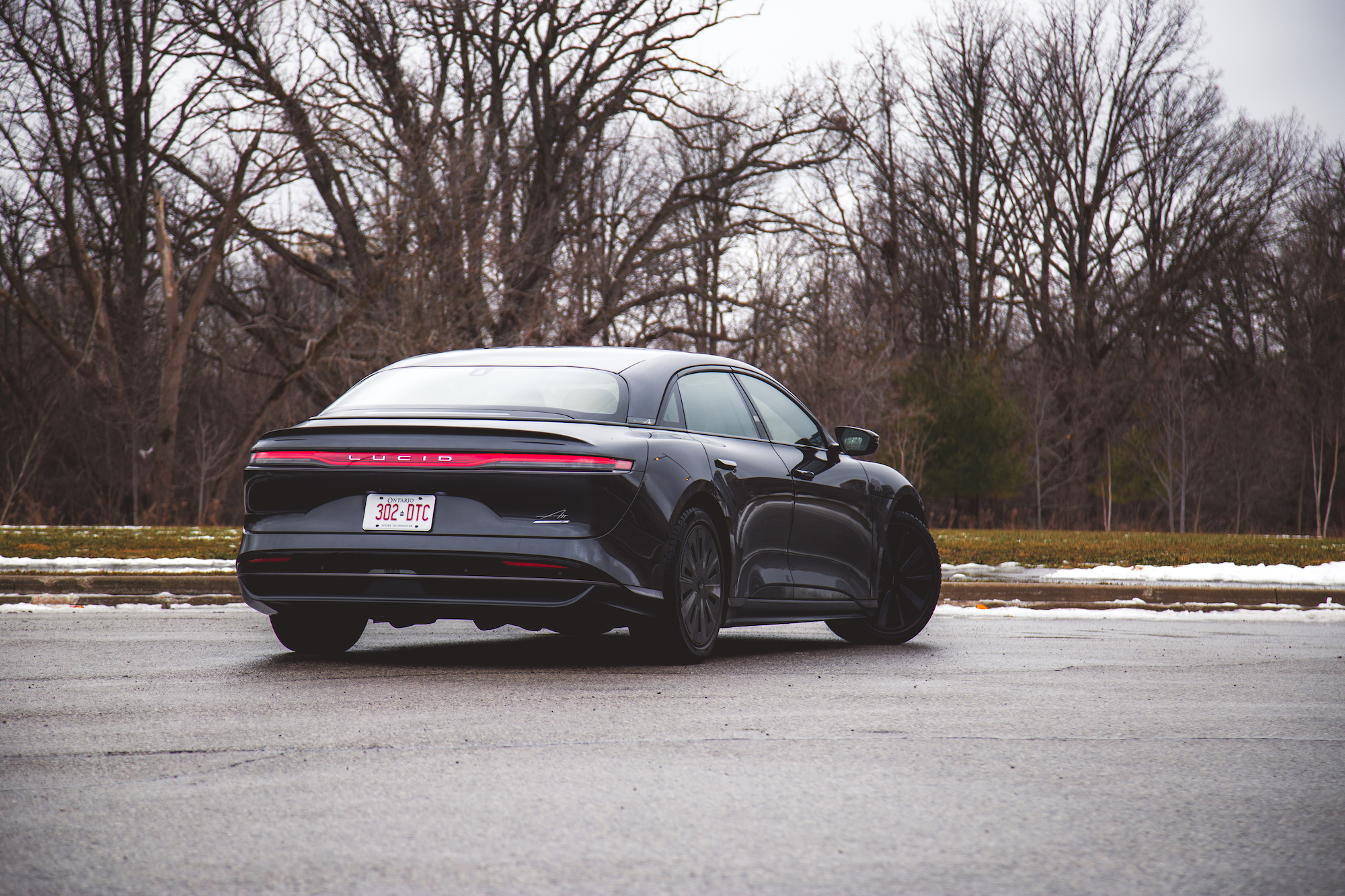 Un coche eléctrico de lujo negro estacionado en una carretera nevada con árboles desnudos al fondo.