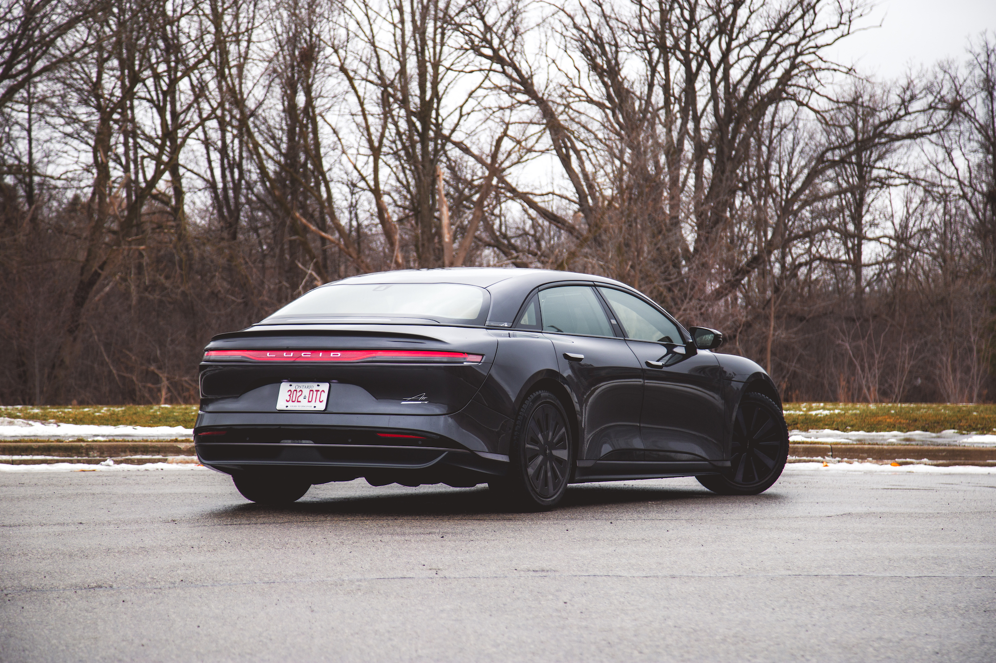 Un sedán eléctrico de lujo negro estacionado en una carretera, mostrando su elegante diseño y su perfil trasero contra un fondo de árboles desnudos.