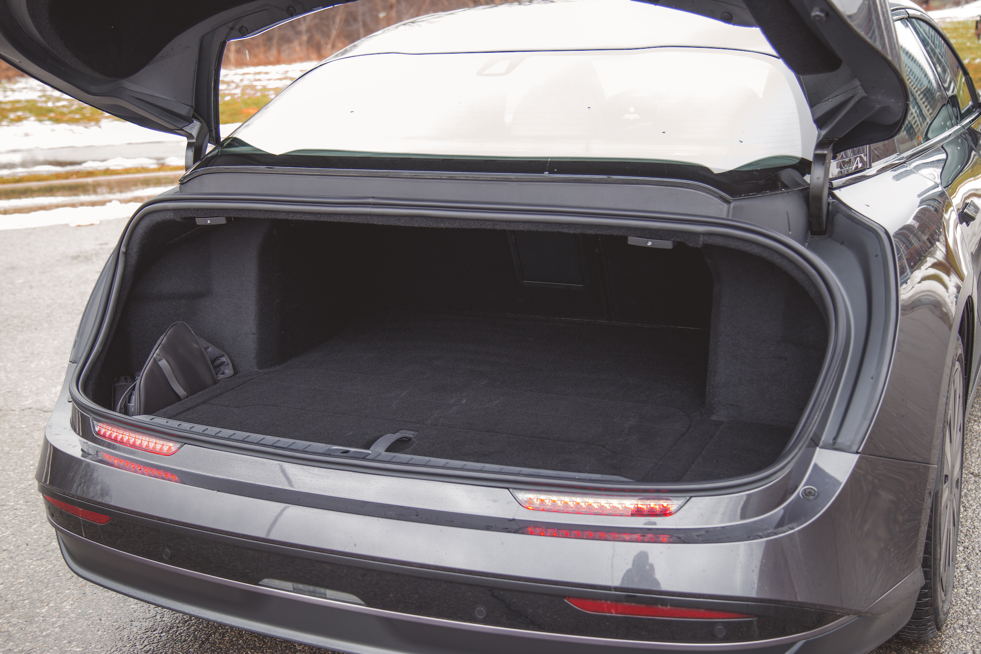 Un maletero abierto de un automóvil gris que muestra un interior espacioso y alfombrado con elementos mínimos.