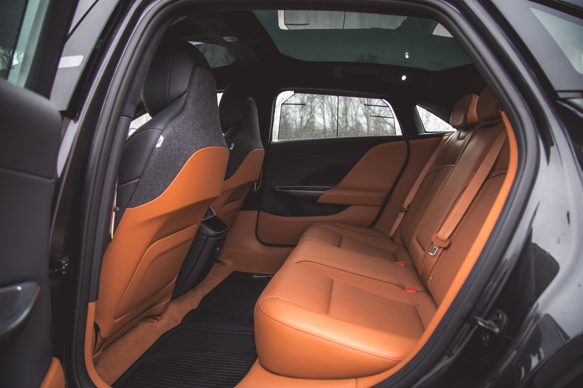 Vista interior de un automóvil que muestra los asientos traseros con tapicería de cuero naranja y detalles en tela oscura.