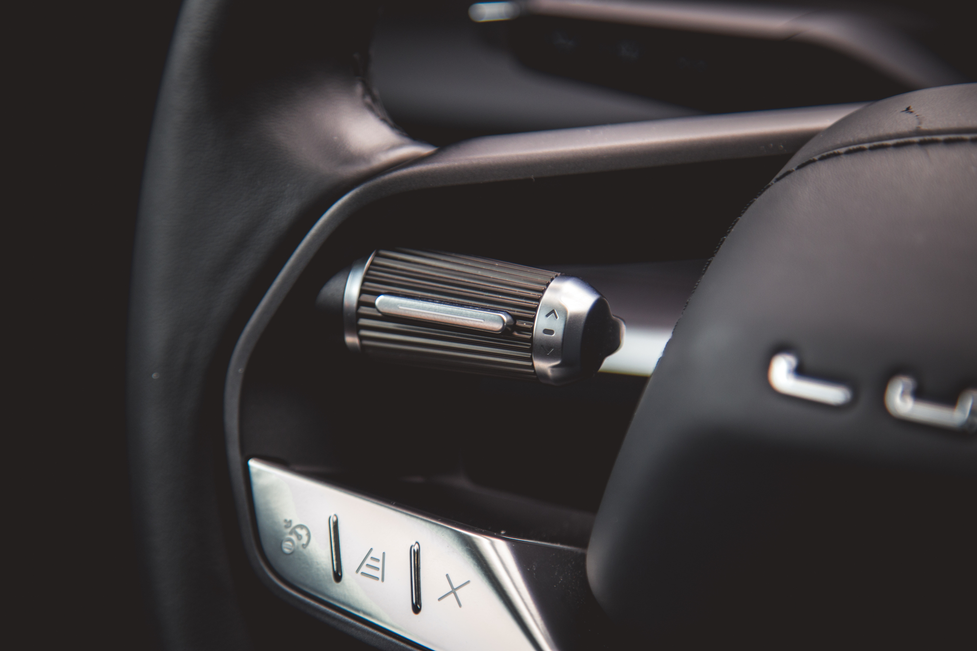 Primer plano de una perilla de control de un automóvil y botones en el tablero, con una superficie texturizada y detalles metálicos.