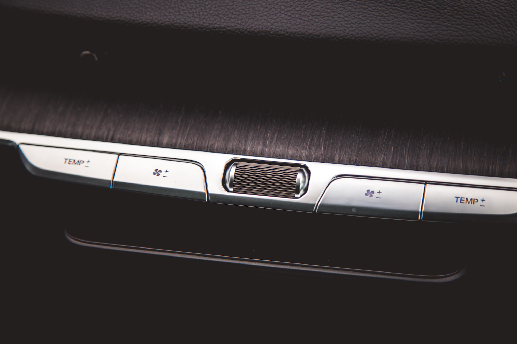 Primer plano del panel de control de temperatura y ventilador de un automóvil con botones marcados como 'TEMP +' y 'TEMP -', junto con ajustes de velocidad del ventilador.