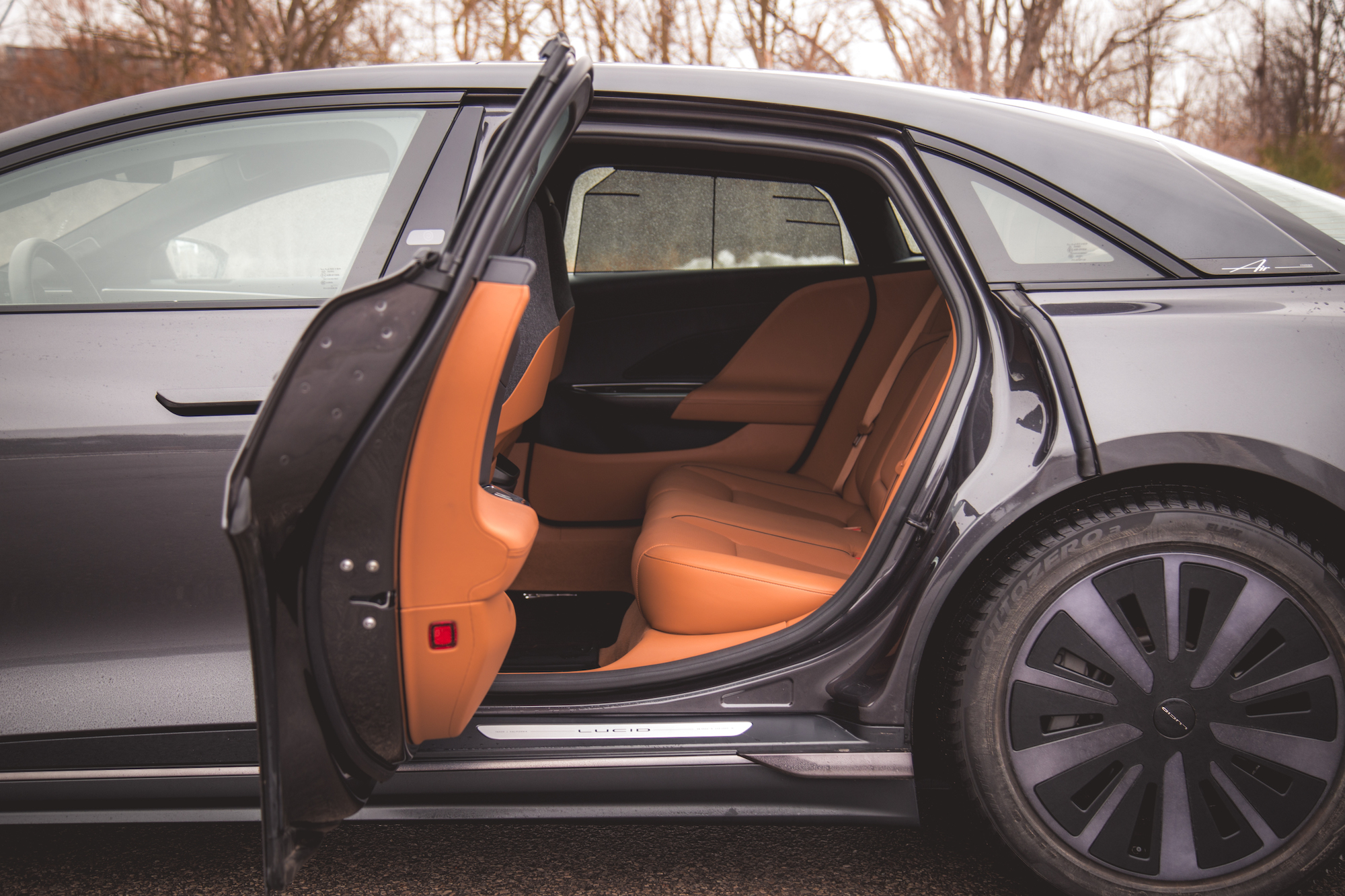 Vista interior de un automóvil de lujo con asientos de cuero marrón, que muestra la puerta trasera abierta.