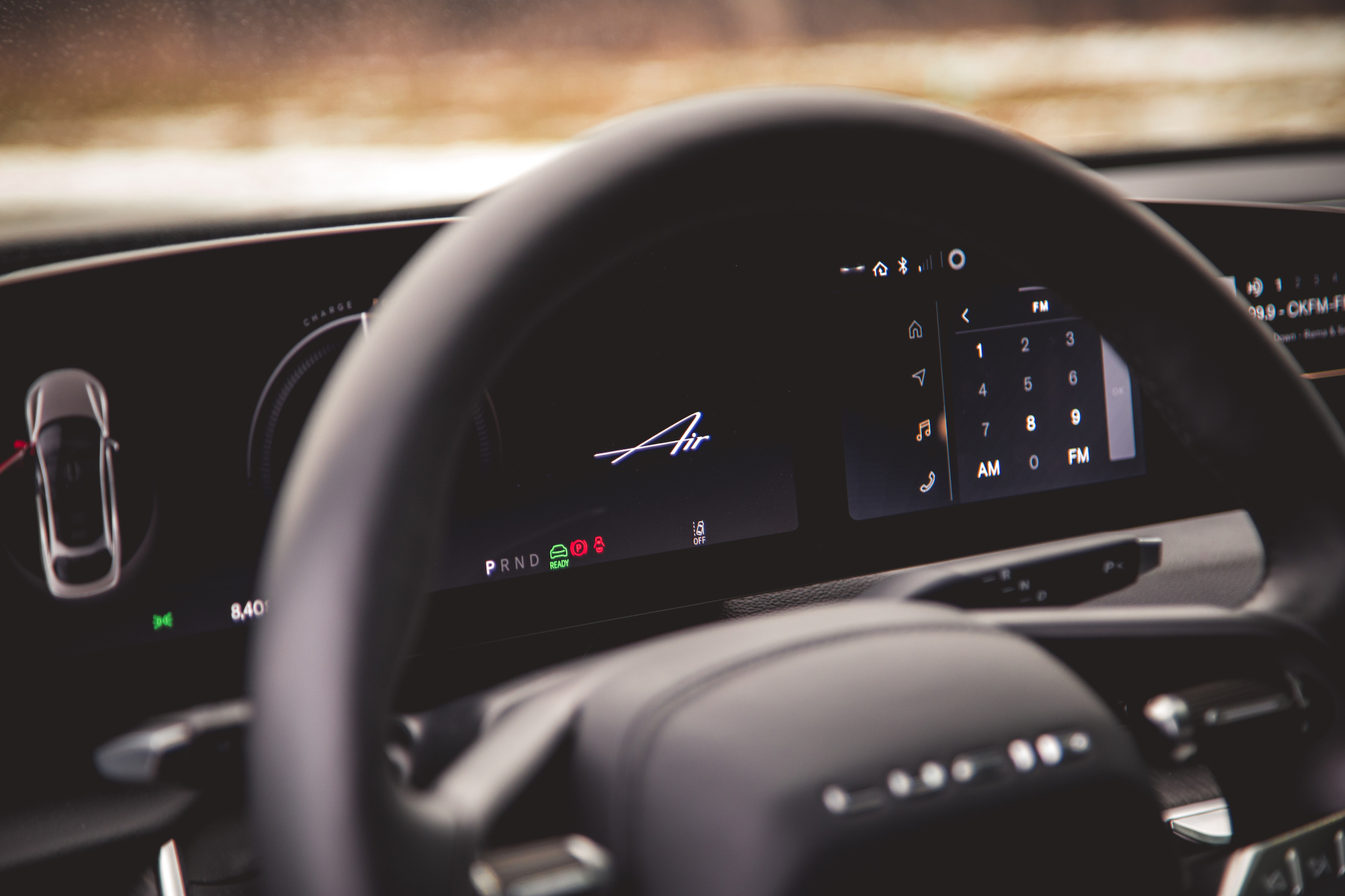 Vista de primer plano del volante y el tablero de un automóvil que muestra información y controles digitales, incluida la selección de marcha, configuraciones de radio y estado de carga.