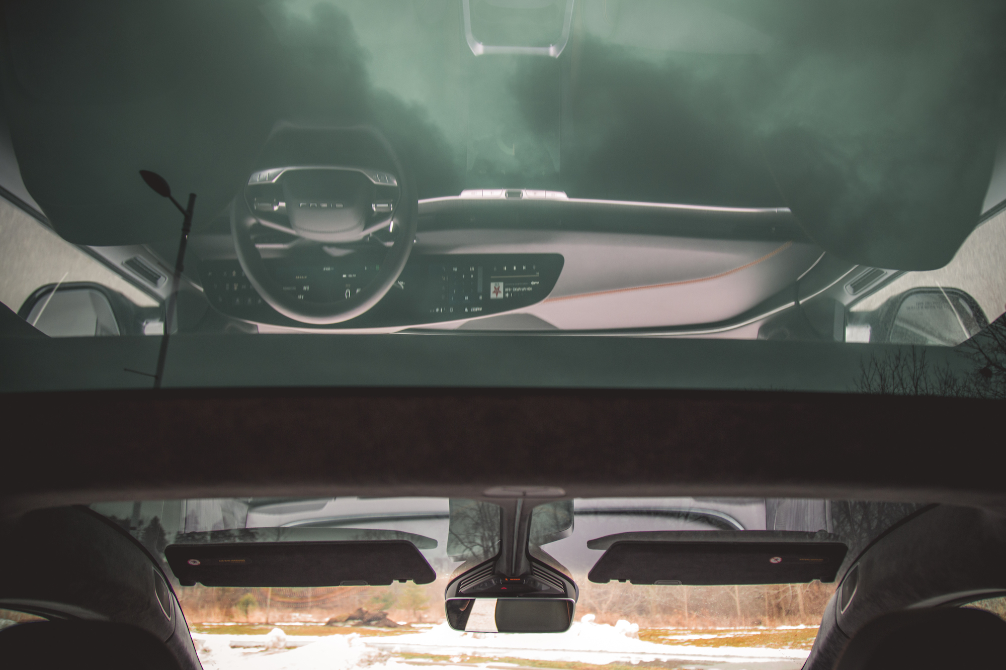 Vista interior del tablero de un automóvil con volante y pantalla táctil, que refleja el cielo nublado a través del parabrisas.