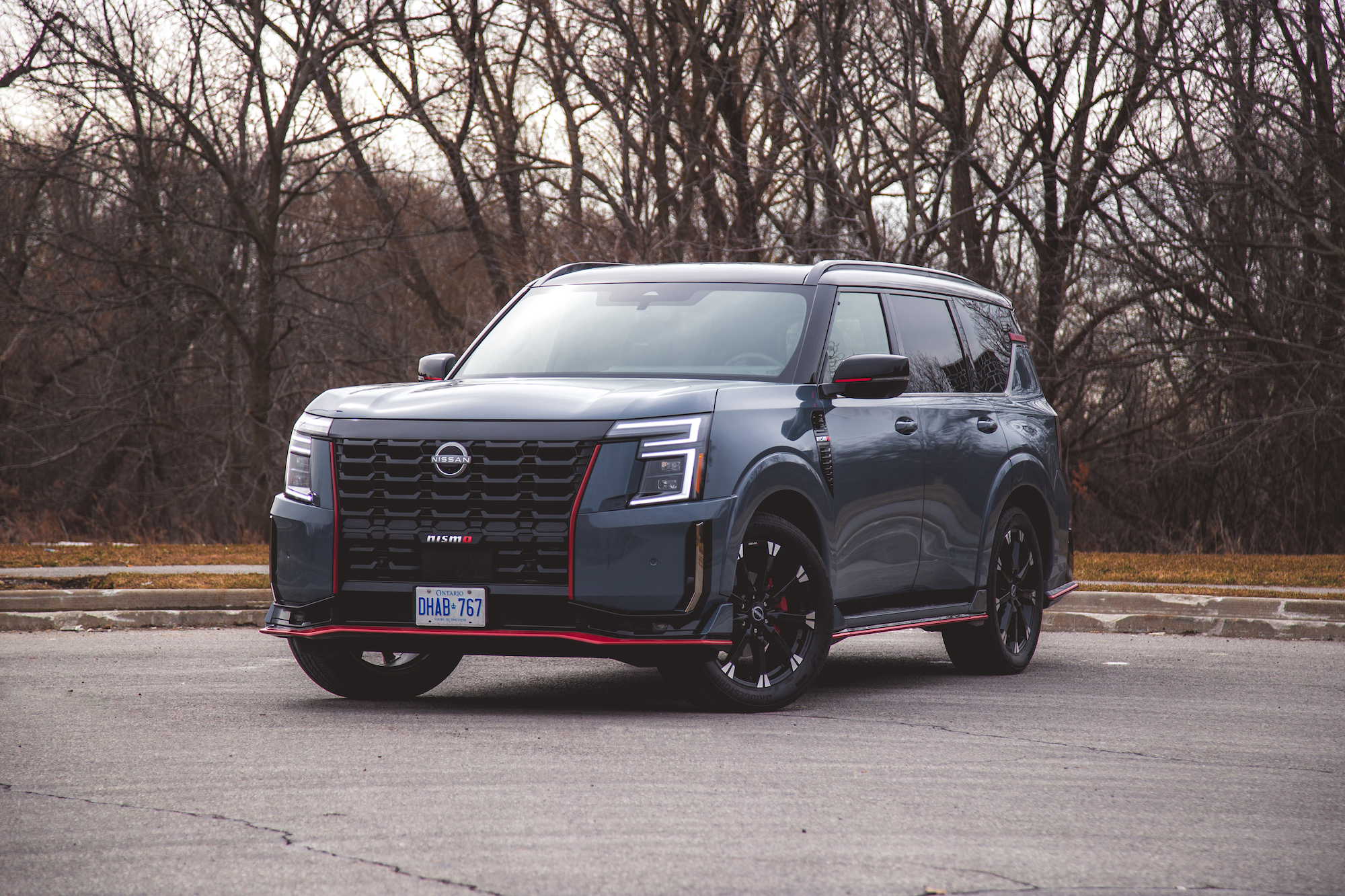 Un vehículo Nissan estacionado en una acera con árboles desnudos al fondo. El automóvil presenta un diseño audaz con una parrilla negra, detalles en rojo y elegantes ruedas negras.