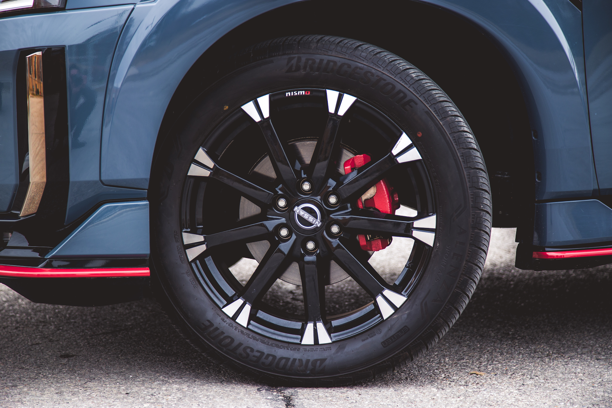 Primer plano de una llanta de aleación negra con detalles plateados, con una pinza de freno roja y un neumático Bridgestone, montada en un vehículo moderno.