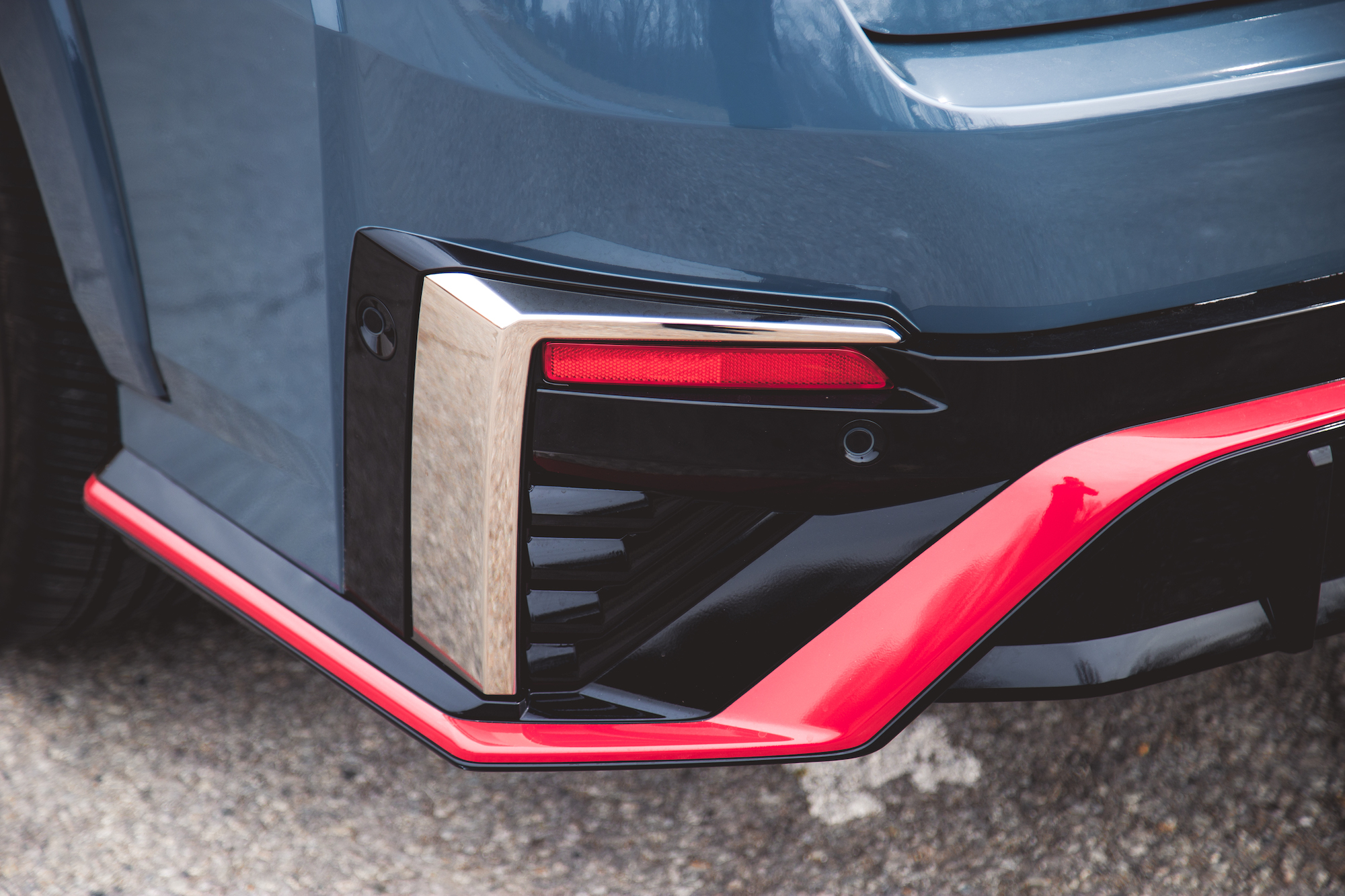 Vista cercana del parachoques trasero de un automóvil que presenta un diseño elegante con acabado metálico y detalles en rojo.