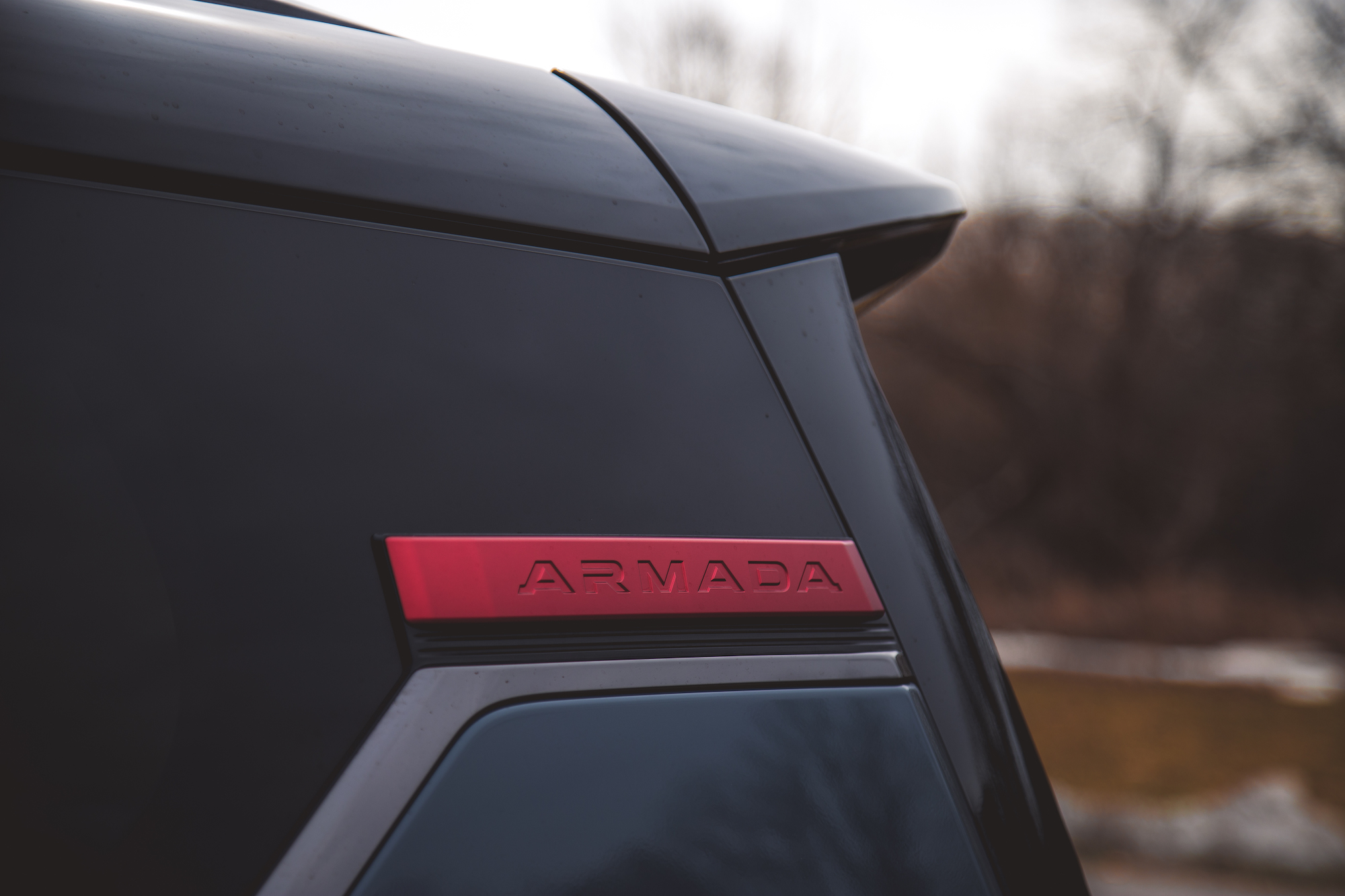 Primer plano de la insignia trasera de un SUV Nissan Armada negro, que muestra las letras rojas 