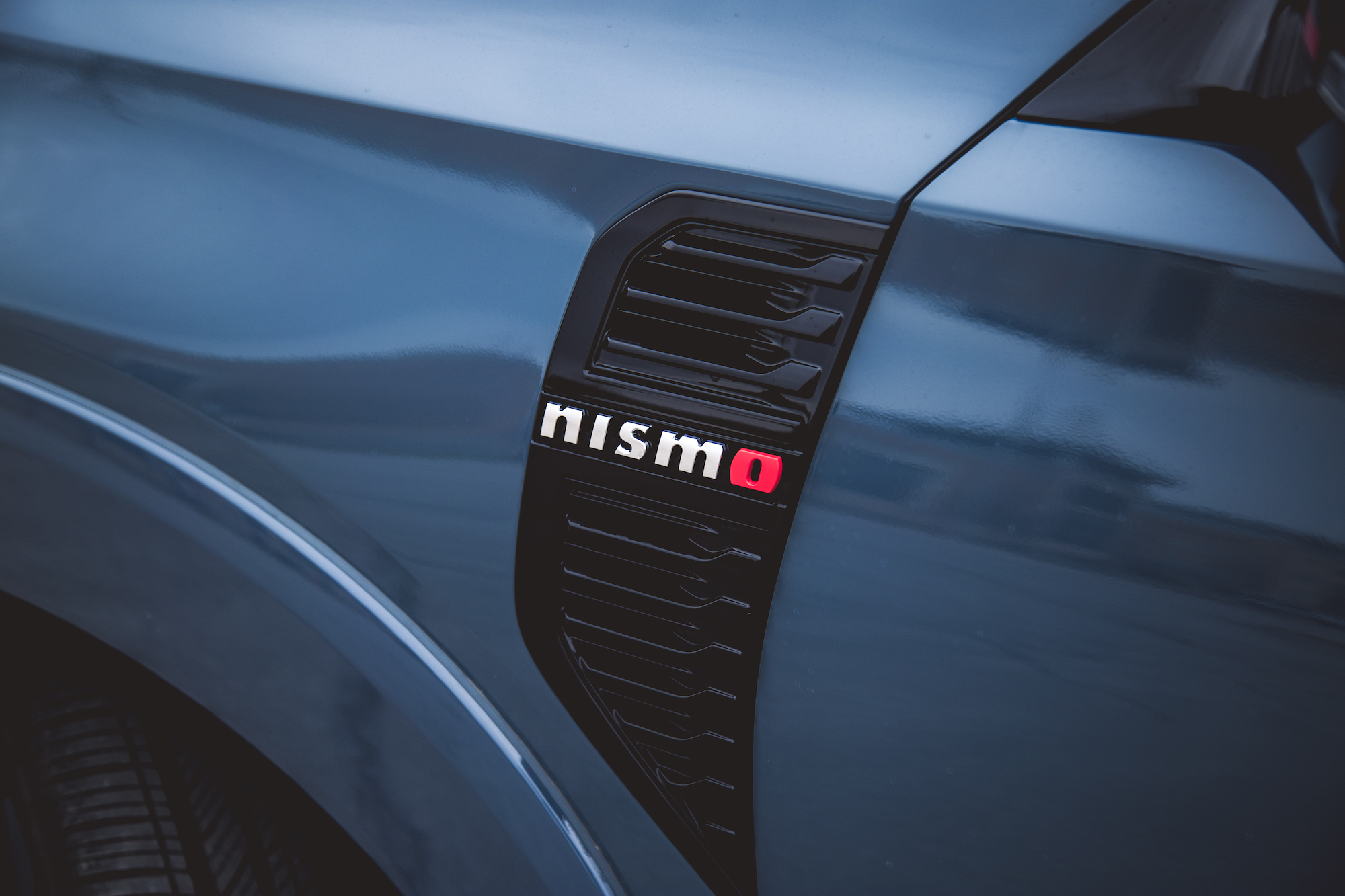 Primer plano del guardabarros de un automóvil que muestra la insignia de Nismo sobre una elegante superficie azul.