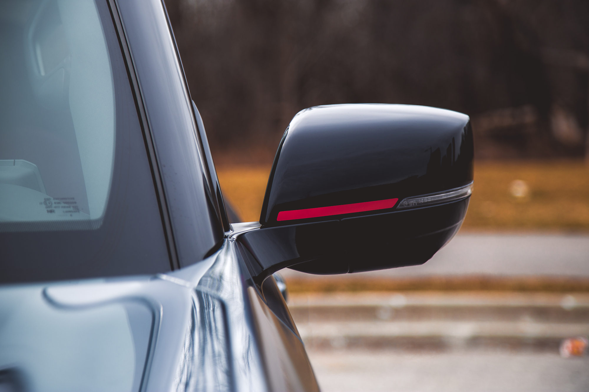 Primer plano del espejo lateral de un automóvil negro con una superficie reflectante y una luz indicadora roja.