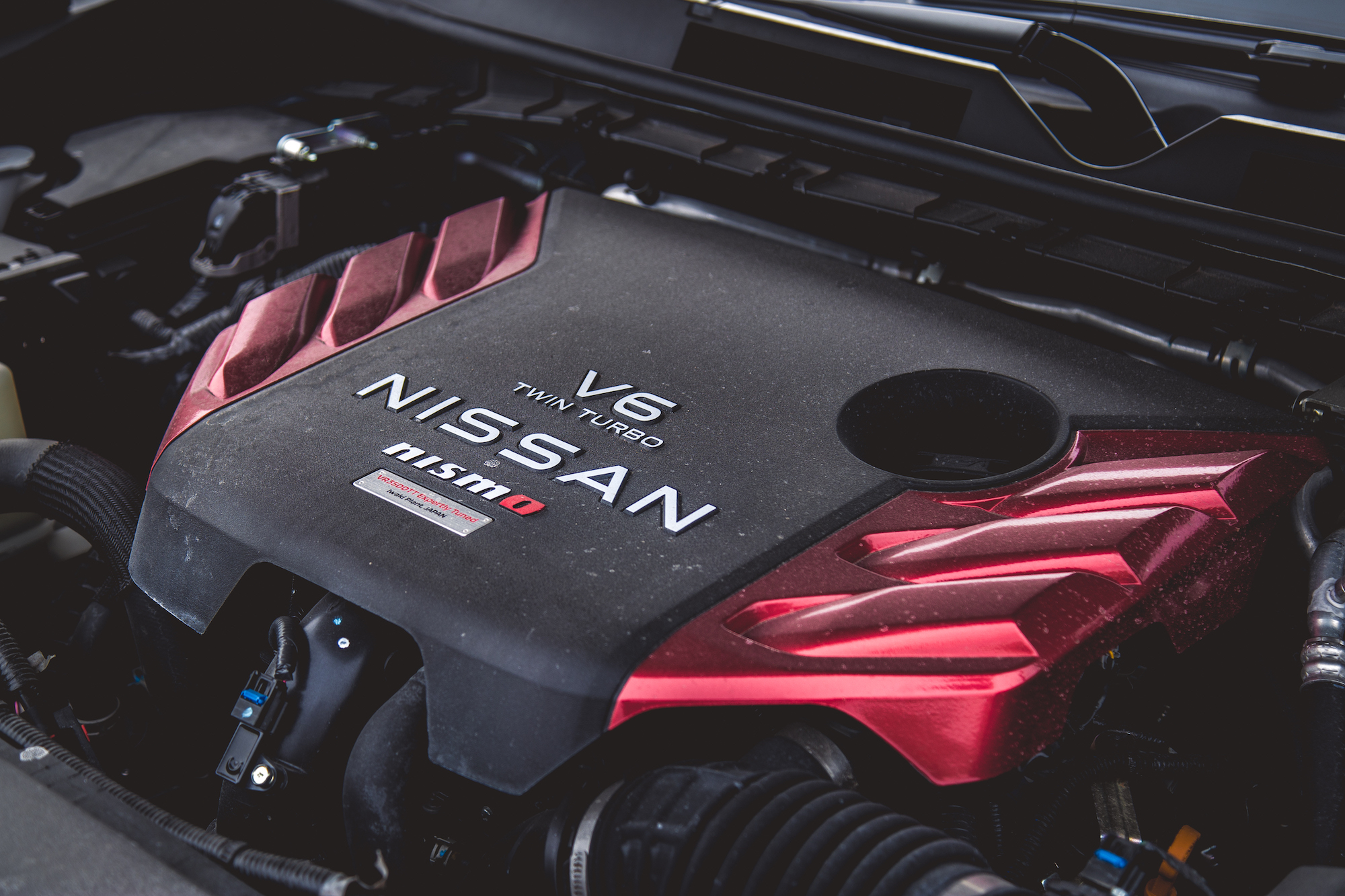 Primer plano de la cubierta del motor Nissan V6 biturbo con la marca Nismo, que muestra un diseño elegante con detalles en rojo.