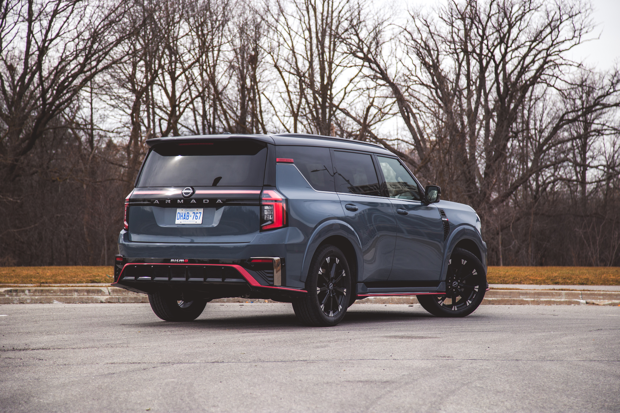 Un Nissan Armada Nismo azul estacionado en una acera con árboles al fondo.