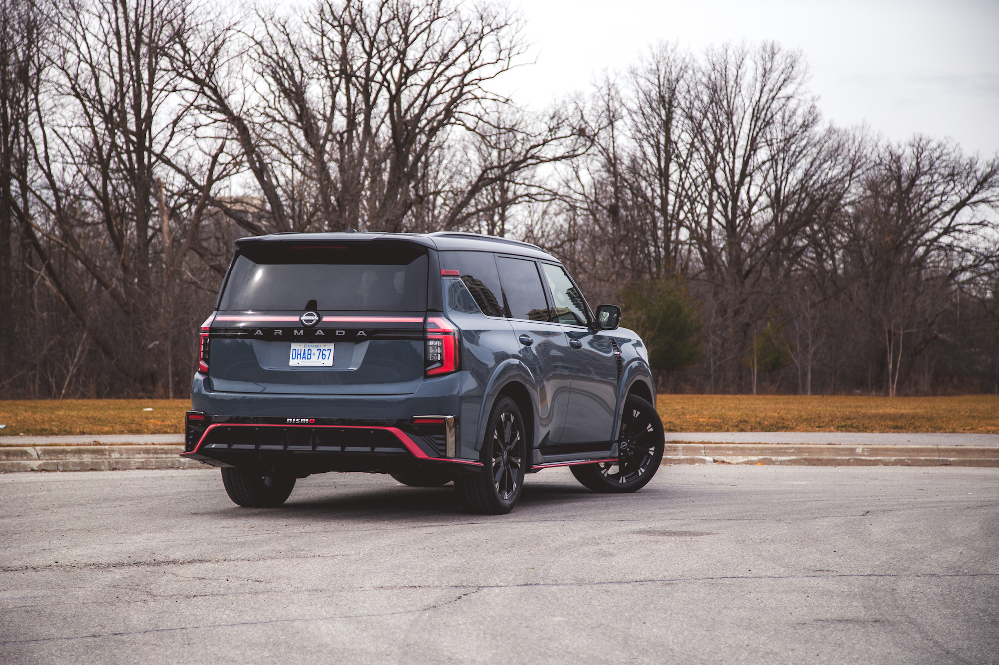 Vista trasera de un Nissan Armada azul estacionado en una carretera, rodeado de árboles desnudos y césped.