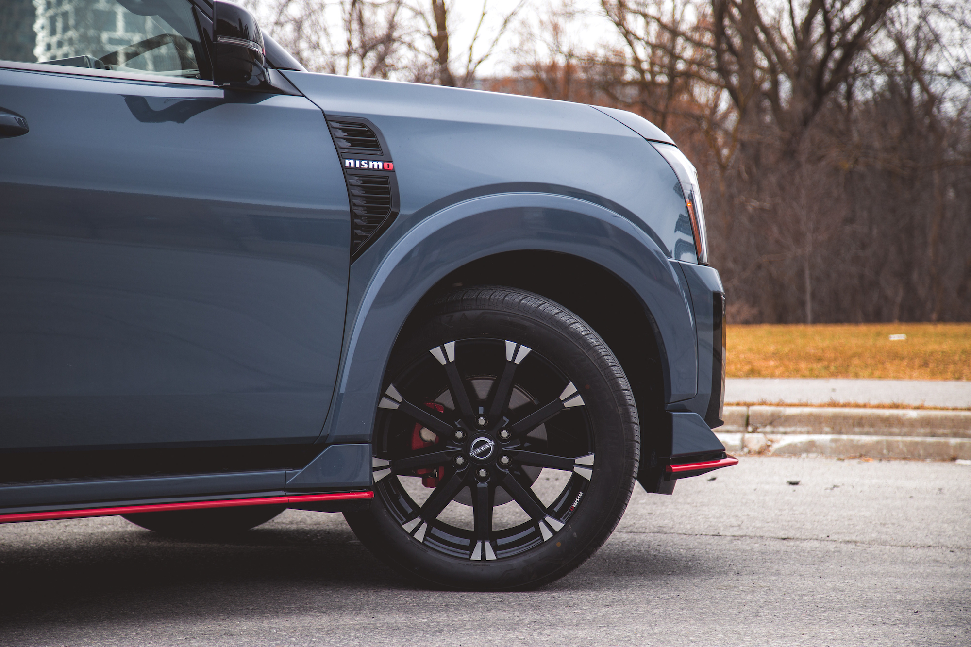 Primer plano de la rueda delantera y el guardabarros de un automóvil azul con una insignia de Nismo, con llantas de aleación negras y detalles decorativos en rojo.