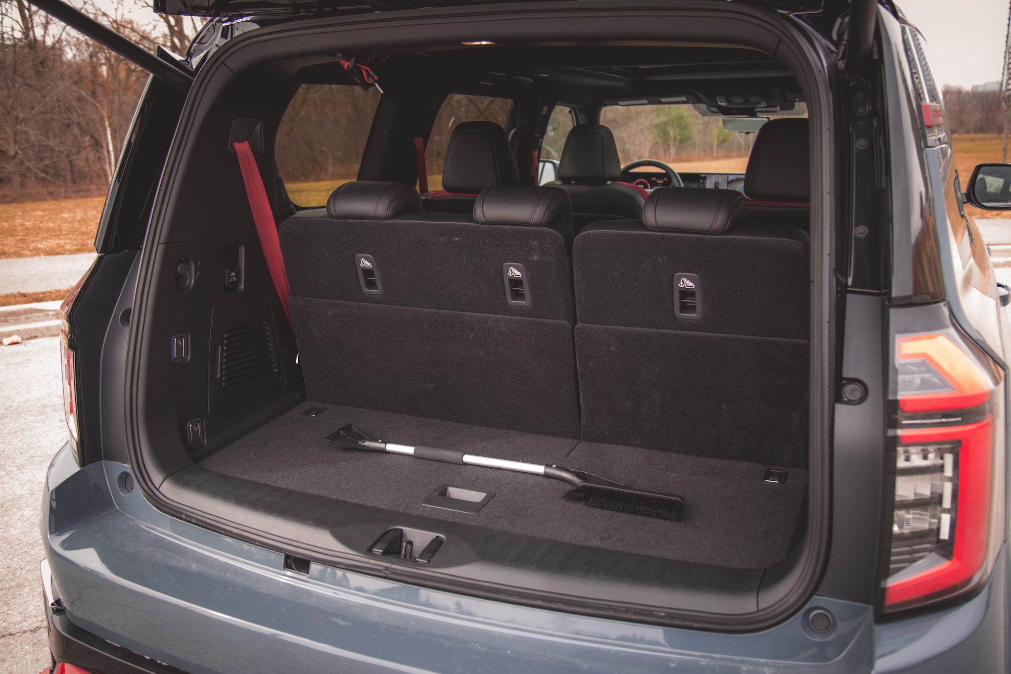 Vista interior del maletero de un vehículo, que muestra dos asientos traseros abatidos y un suelo enmoquetado negro con una herramienta de limpieza apoyada sobre él.