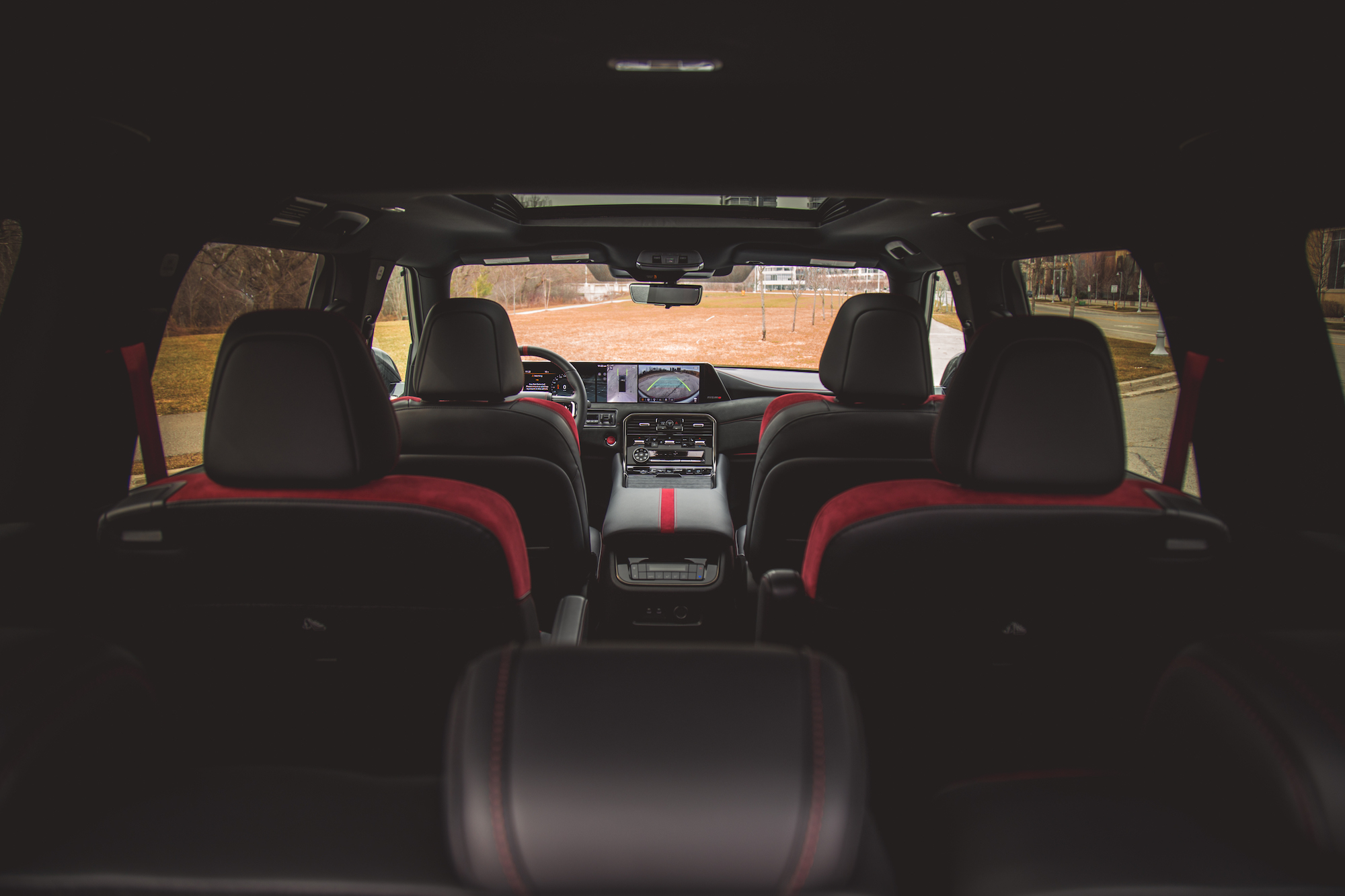 Vista interior de un automóvil moderno que muestra los asientos delanteros, el tablero y el techo corredizo panorámico, con tapizado negro y rojo.