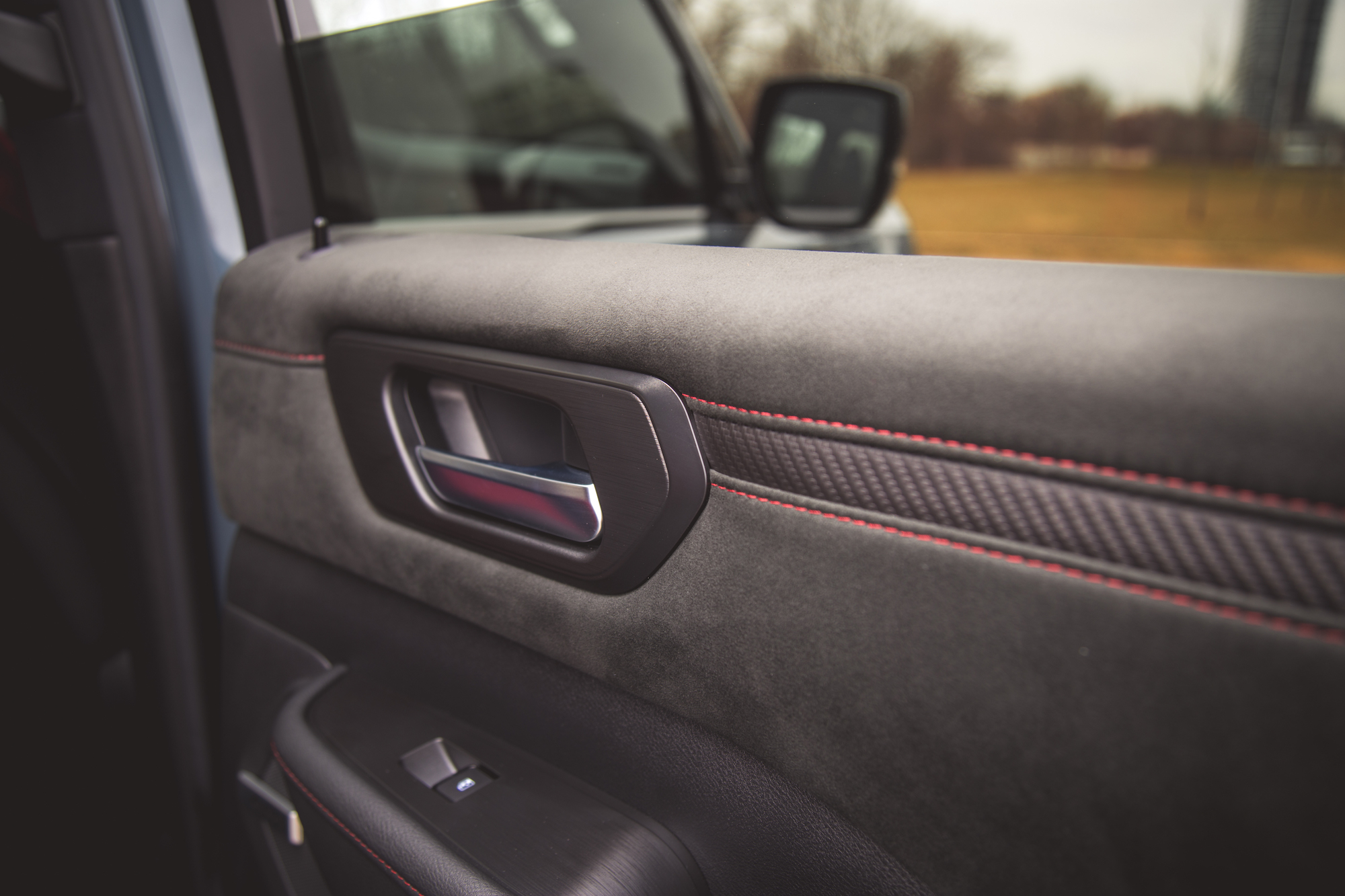 Vista en primer plano del interior de la puerta de un automóvil con textura de gamuza, manija metálica y costuras rojas a lo largo de la costura.