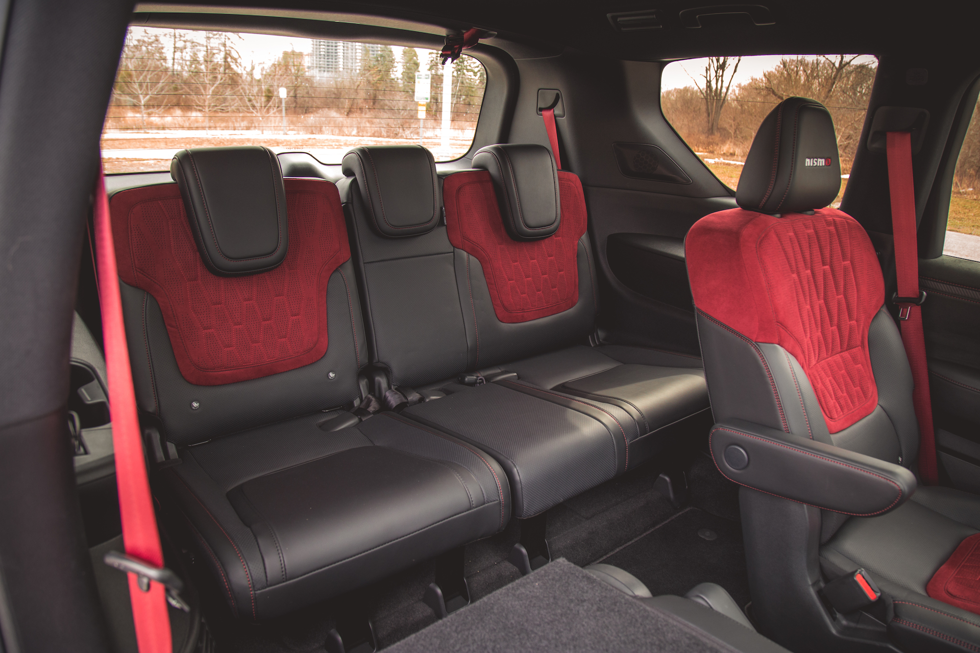 Vista interior del asiento trasero de un vehículo con tapizado negro y rojo, que incluye tres posiciones de asiento con reposacabezas.