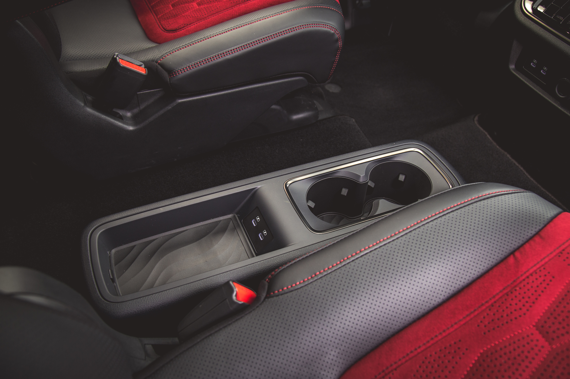 Vista cercana del interior de un automóvil con asientos negros y rojos, con una consola central que muestra un portavasos y botones de control.