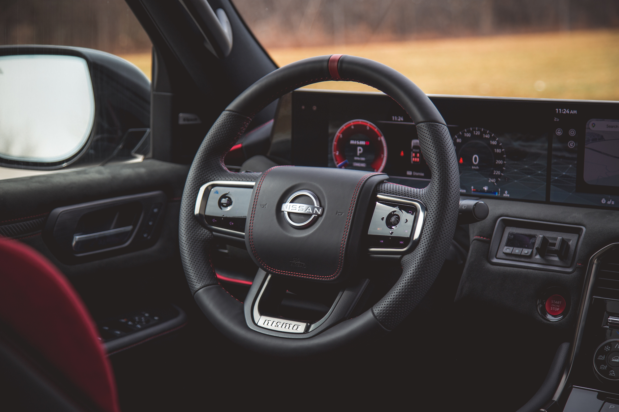 Vista cercana del interior de un automóvil Nissan que presenta un volante deportivo con controles, un tablero con pantalla digital y una palanca de cambios. El interior tiene una combinación de detalles en negro y rojo.