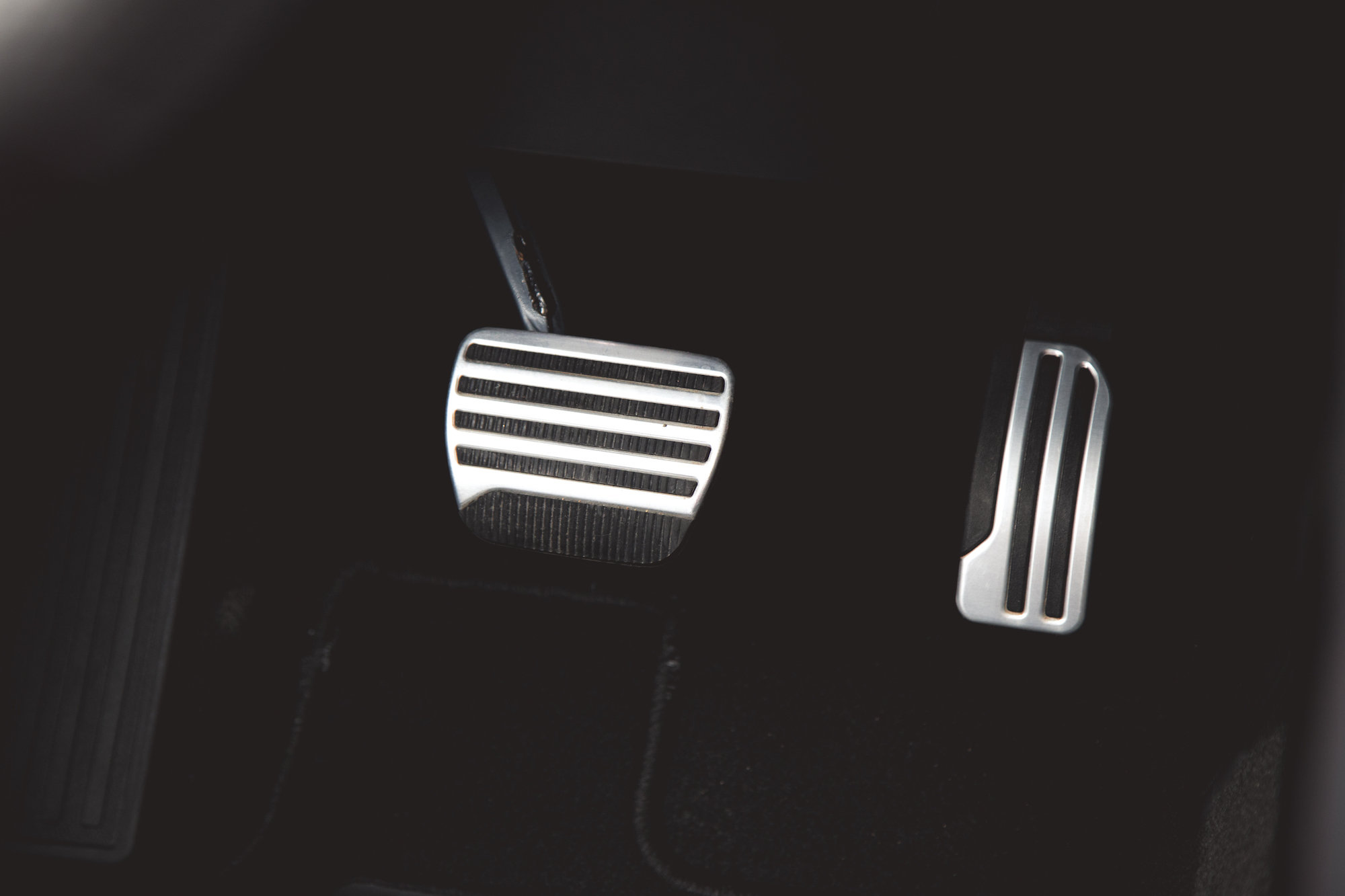 Vista cercana de los pedales de un automóvil, con un pedal de freno metálico con ranuras y un pedal de acelerador plateado.