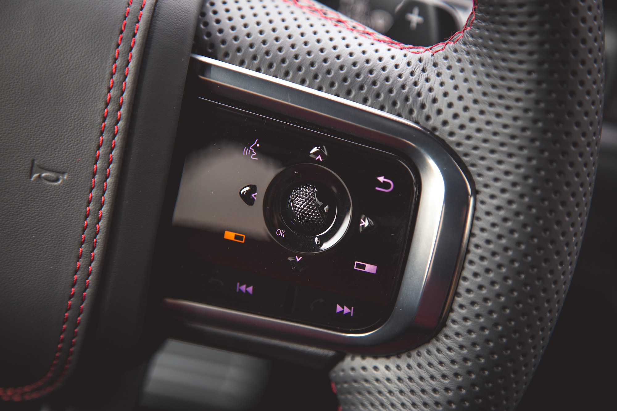 Primer plano del panel de control del volante de un automóvil con varios botones y un dial texturizado.