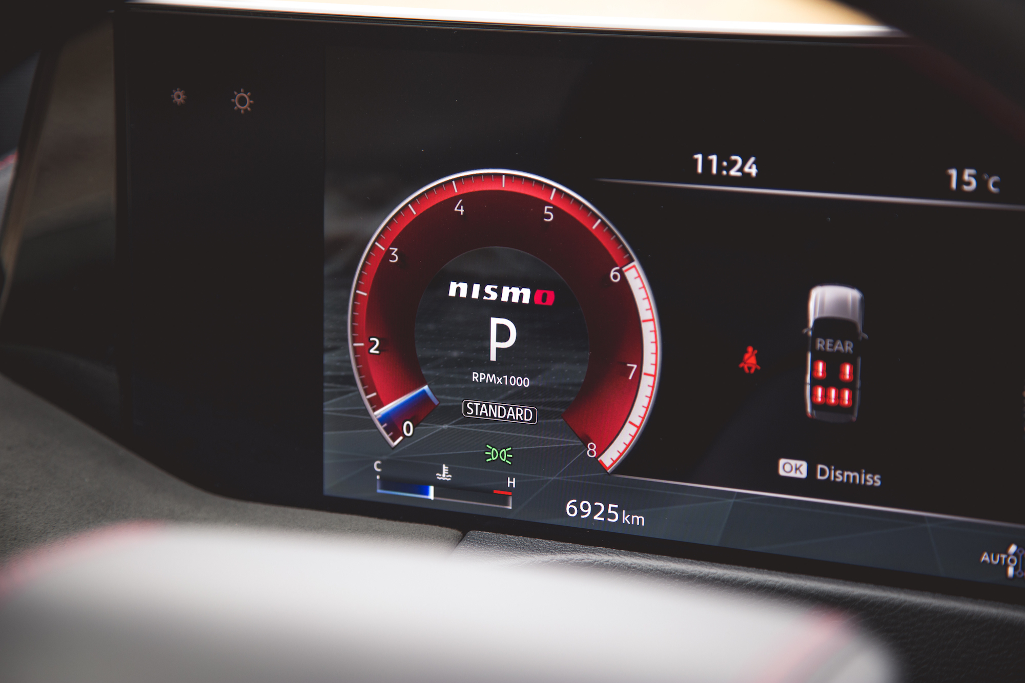 Primer plano del tablero de un automóvil que muestra un medidor digital con indicador de RPM, con la marca 'Nismo', la posición de marcha 'P' y varios íconos de estado del vehículo.