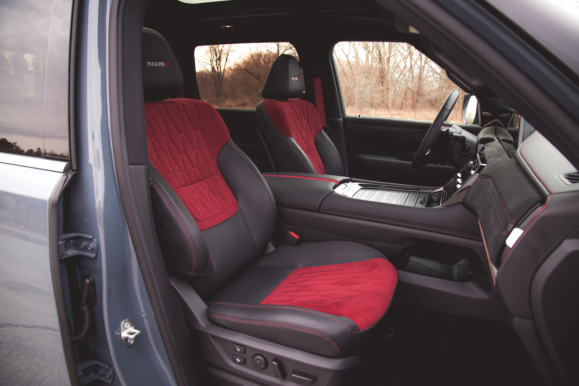 Vista interior de un vehículo que muestra dos asientos deportivos con tapizado, tablero y volante de color rojo y negro.