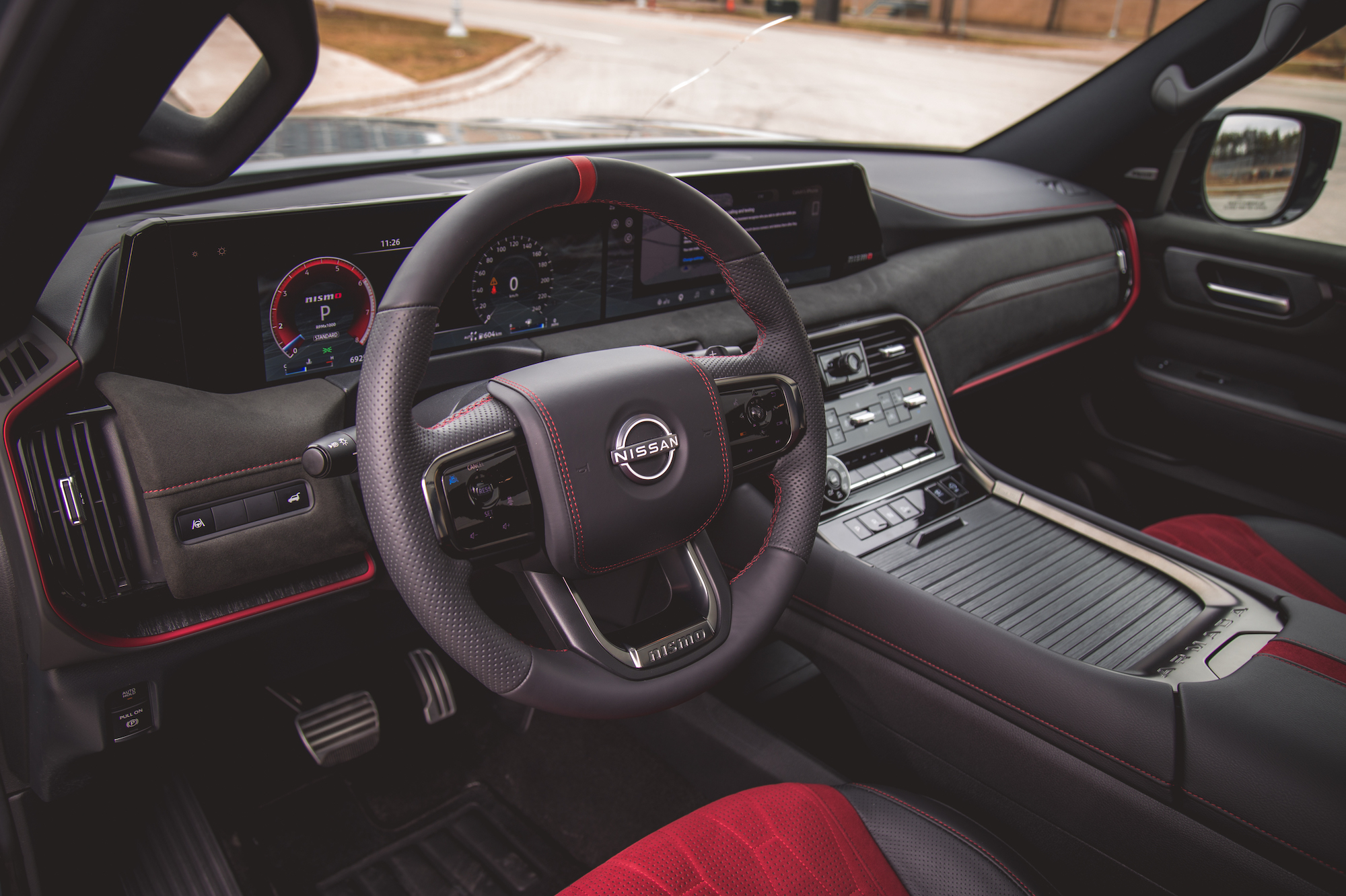 Vista en primer plano del interior de un vehículo Nissan, que presenta un elegante volante con el logotipo de Nissan, una pantalla de tablero digital y un moderno diseño de consola central con detalles en rojo.