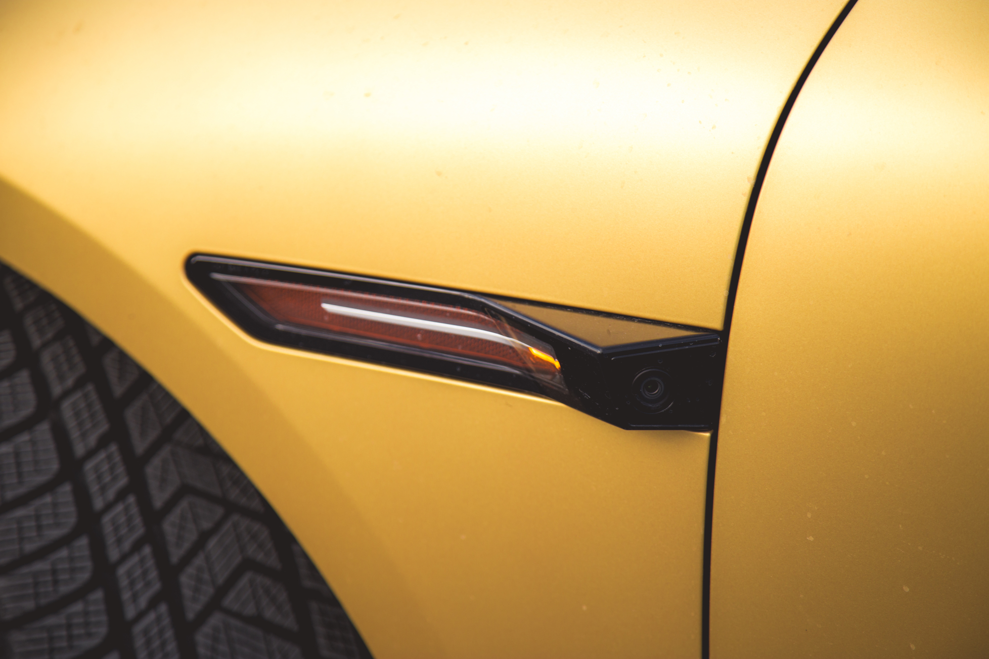 Primer plano del espejo lateral de un automóvil amarillo que muestra una señal de giro y una cámara.