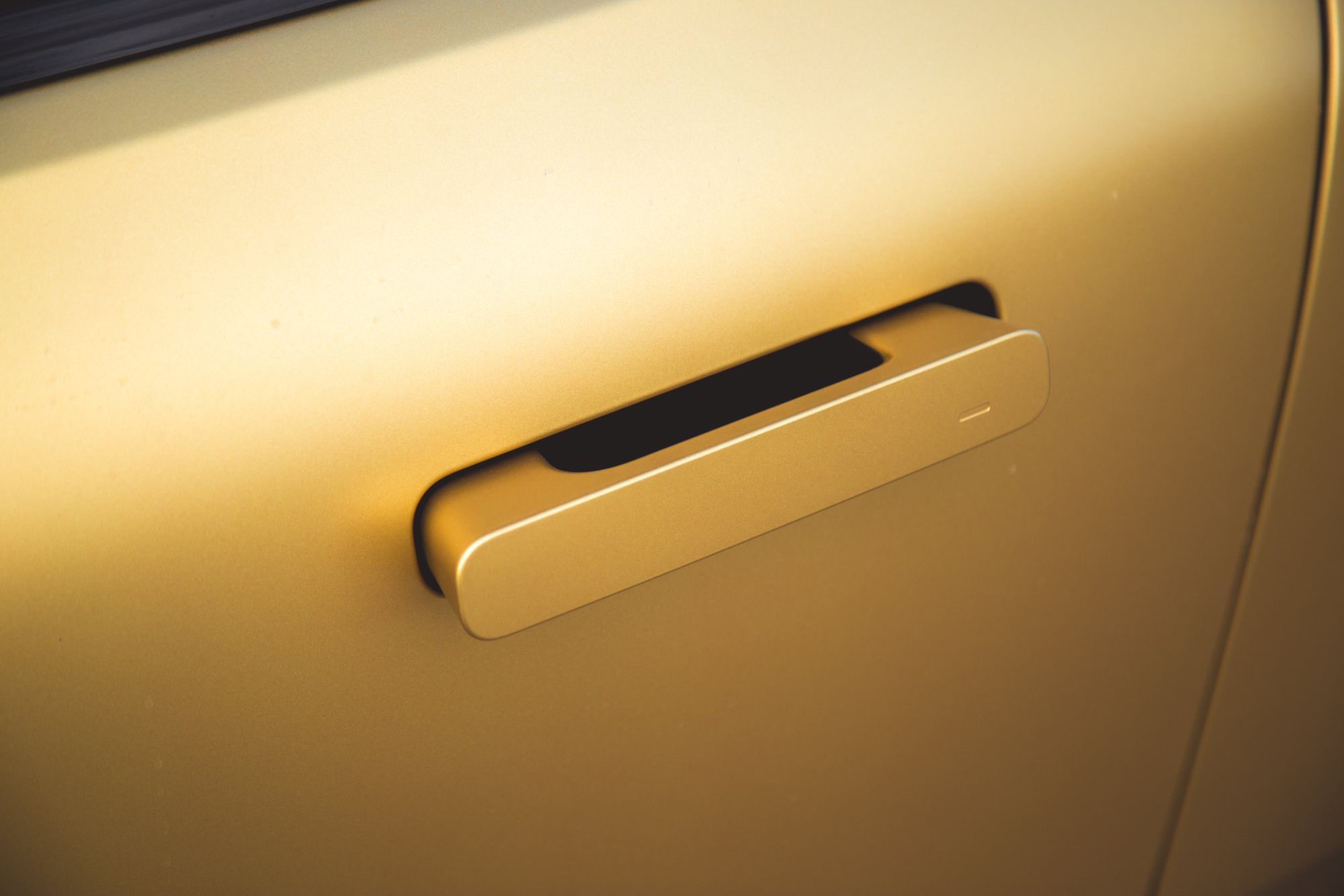 Primer plano de la manija de la puerta de un automóvil moderno sobre una superficie de color dorado.