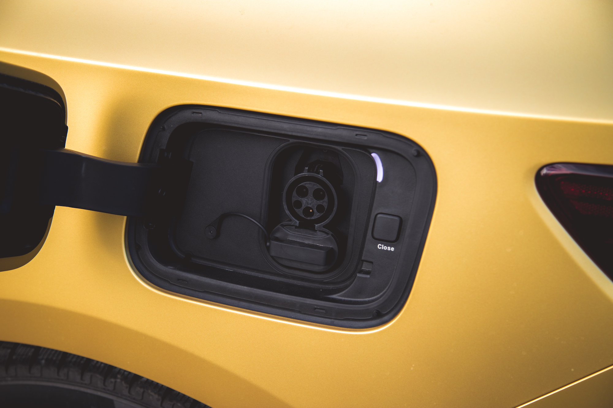 Primer plano de un puerto de carga de un coche eléctrico en un vehículo amarillo, que muestra el conector y el mecanismo de cierre.