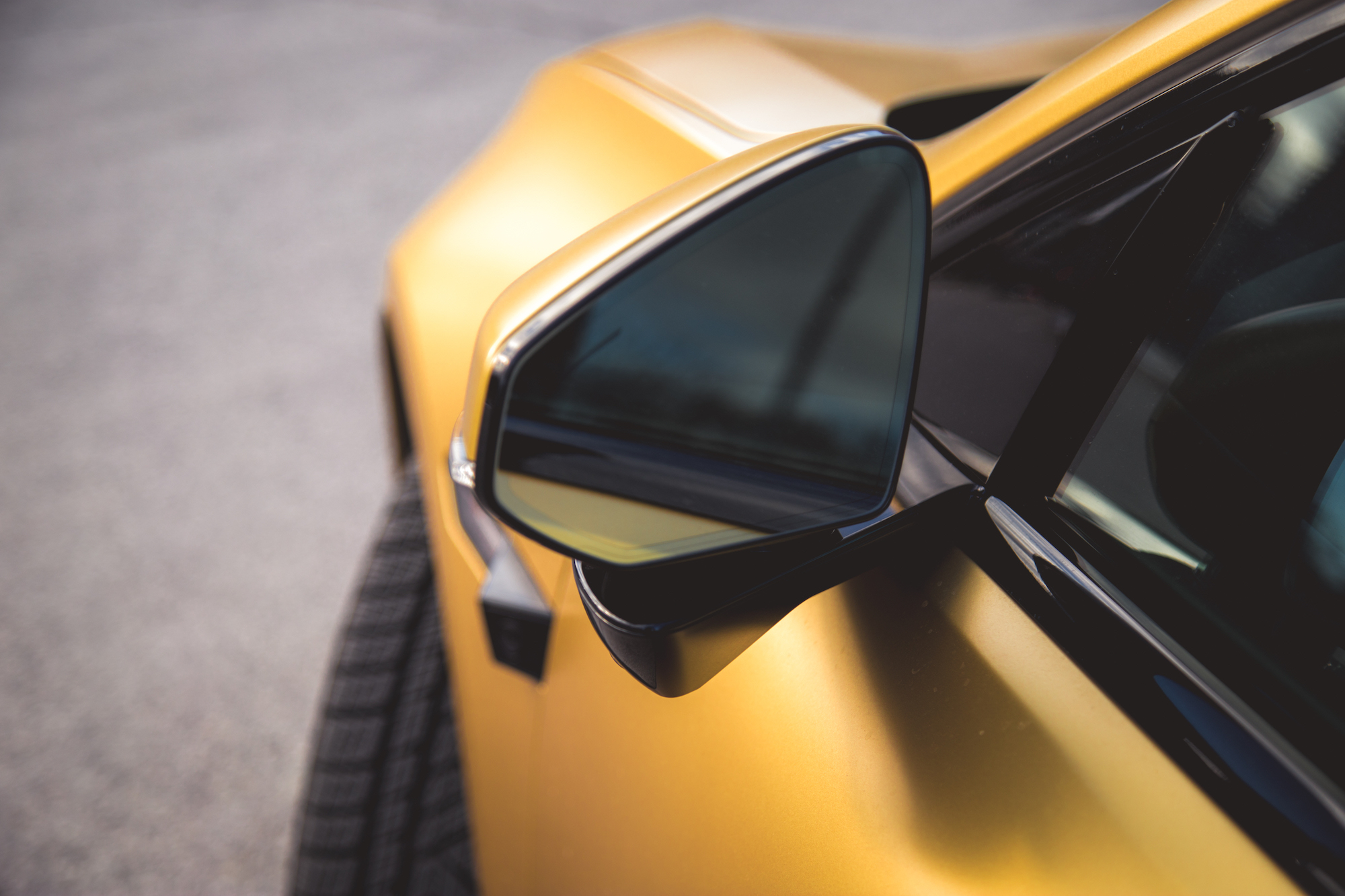 Primer plano de un espejo lateral en un auto deportivo amarillo, destacando el diseño elegante y el acabado brillante.