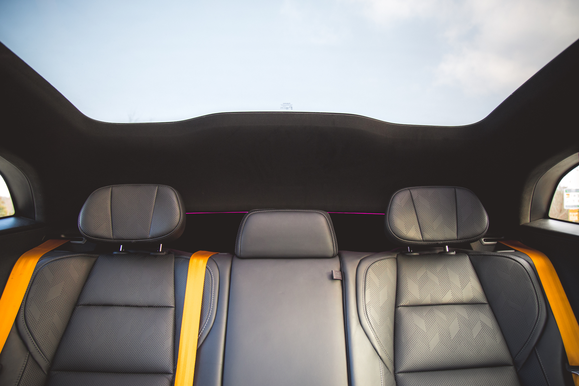 Vista interior del asiento trasero de un automóvil con tapicería de cuero negro, reposacabezas y techo corredizo panorámico.