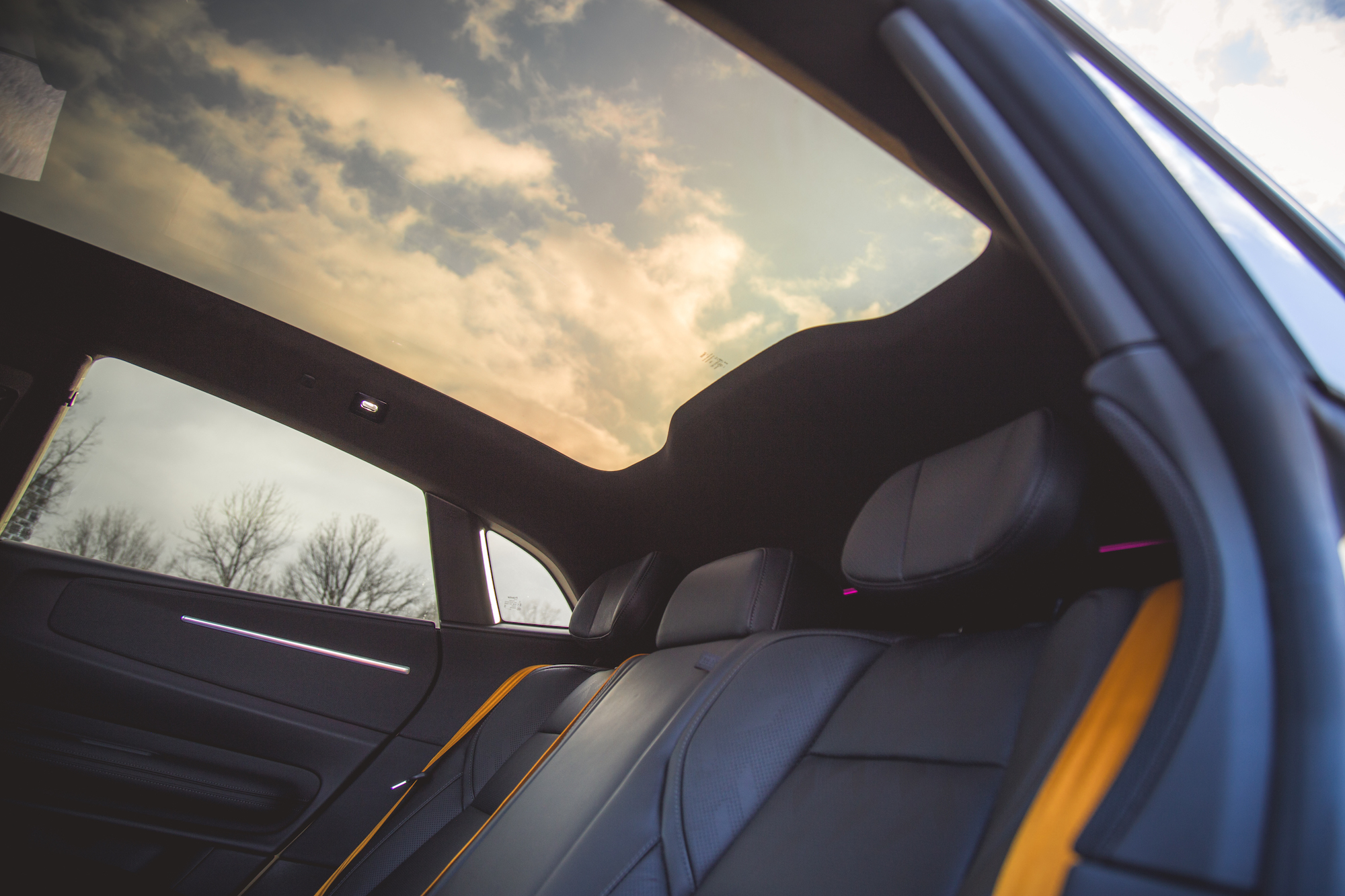 Vista interior de un automóvil que exhibe elegantes asientos de cuero negro y un techo corredizo panorámico que refleja las nubes.
