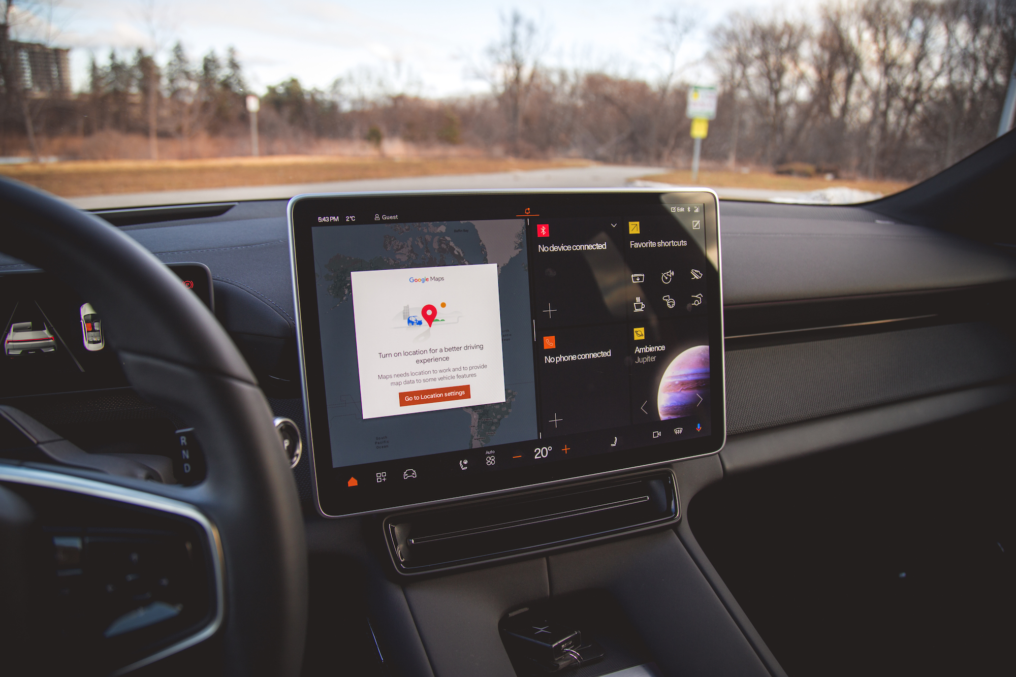 Vista interior del tablero de un automóvil con una gran pantalla táctil que muestra Google Maps con un mensaje de ubicación y varios íconos y controles de aplicaciones.